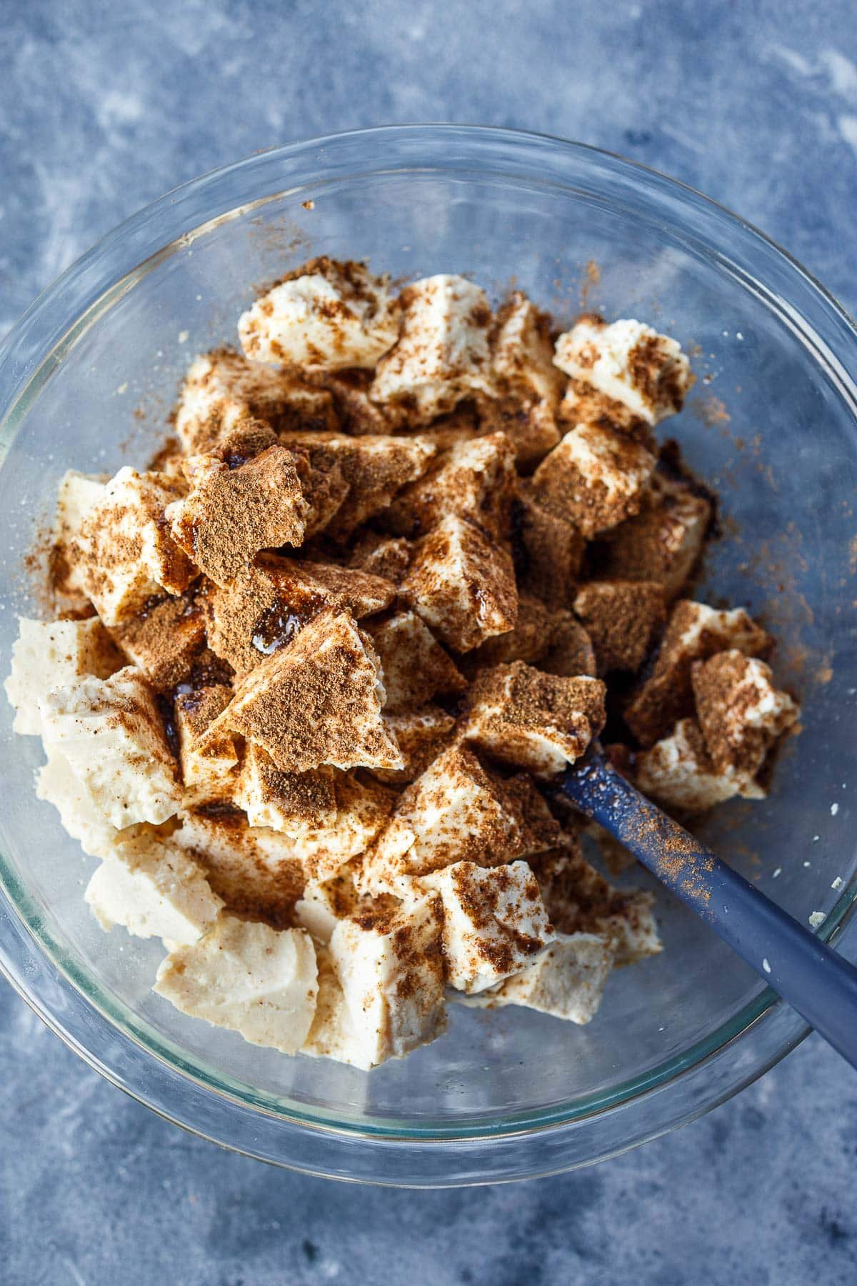glass mixing bowl with torn tofu tossed with spices.