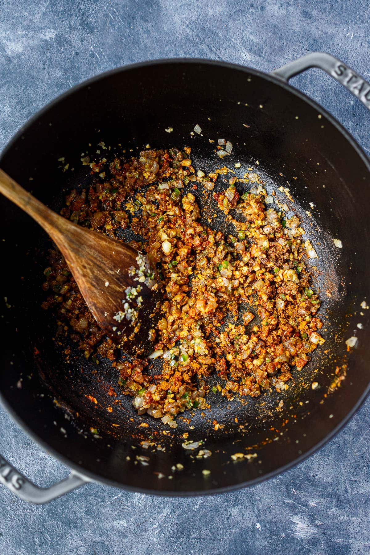 wood spatula stirring aromatics in spices in dutch oven to make the base for butter tofu sauce.