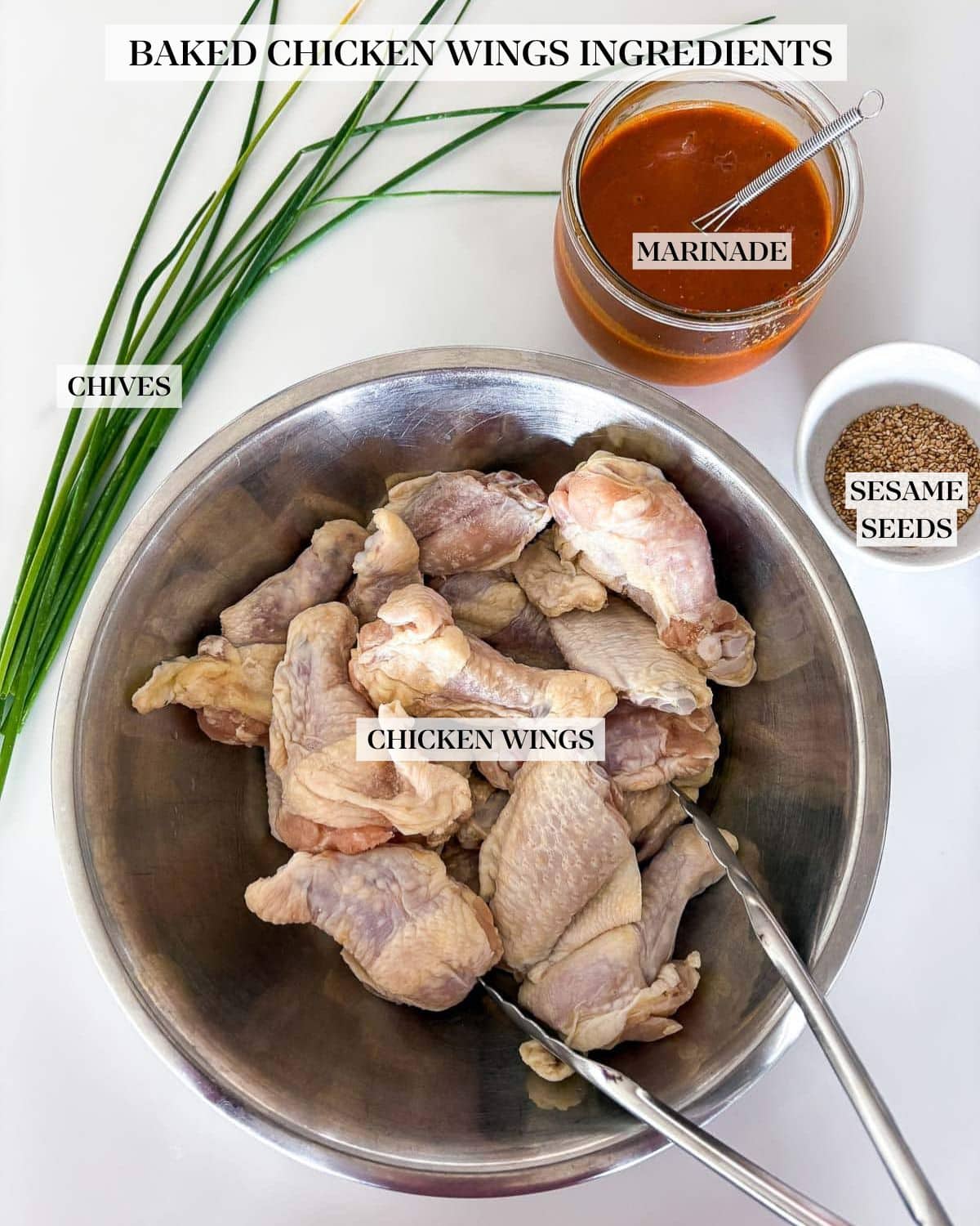 ingredients for sticky Asian chicken wings - chives, jar of marinade, bowl of toasted sesame seeds, metal mixing bowl with chicken wings and tongs. 