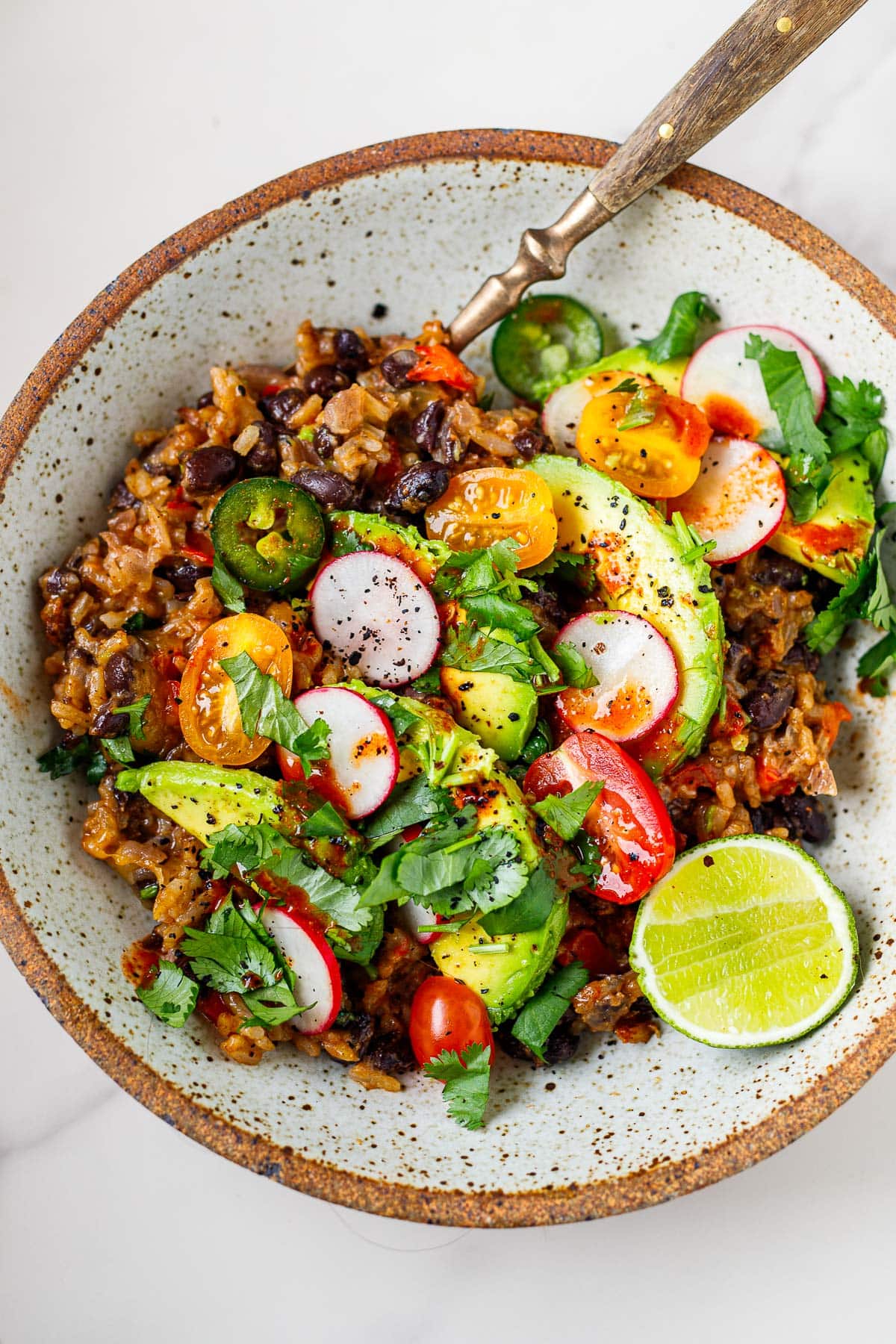 bowl of cheesy rice and beans topped with jalapeno, cherry tomatoes, radish, avocado, lime, cilantro, and hot sauce.