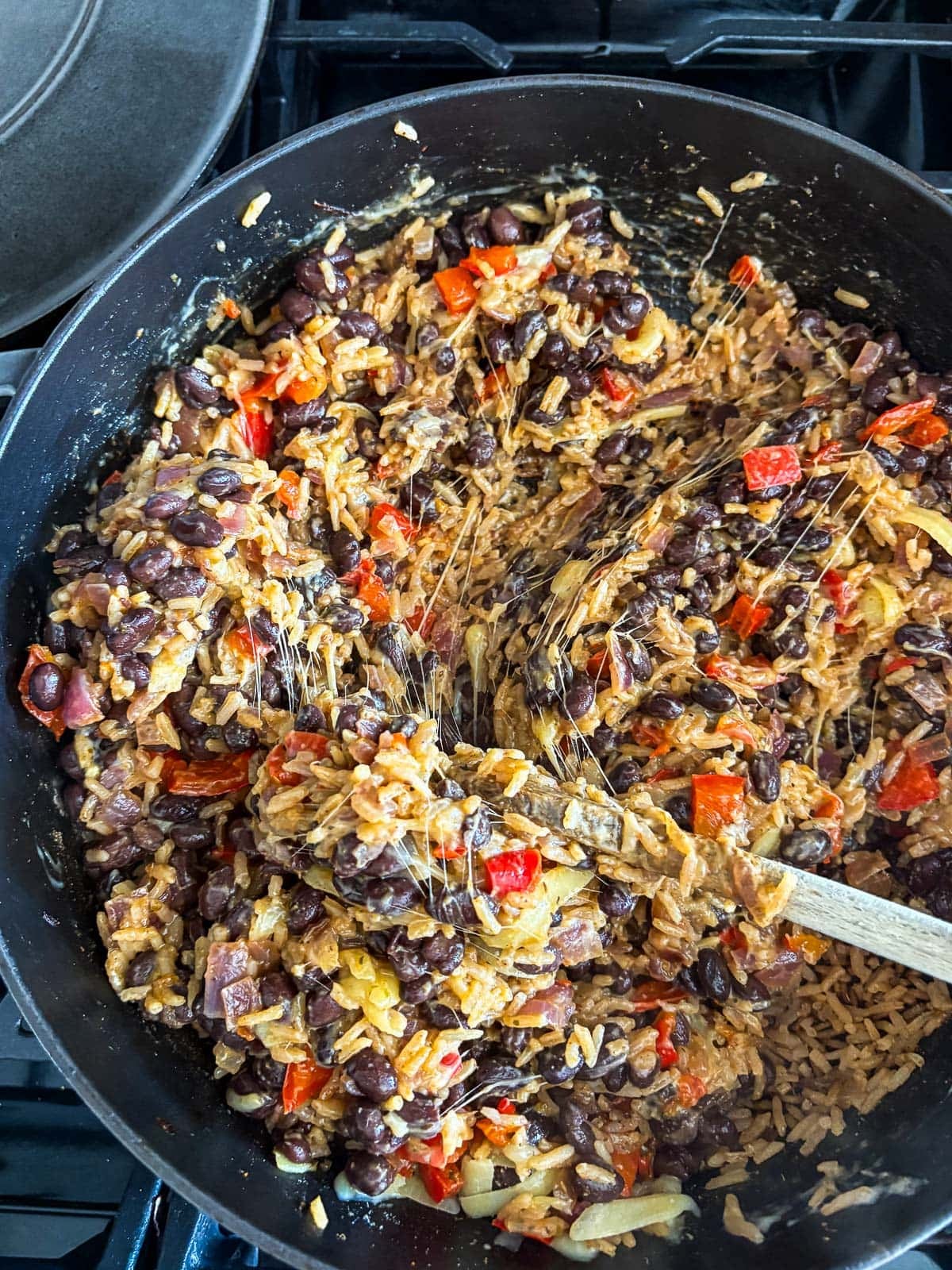 wood spoon stirring cheesy rice and beans with veggies in pot.