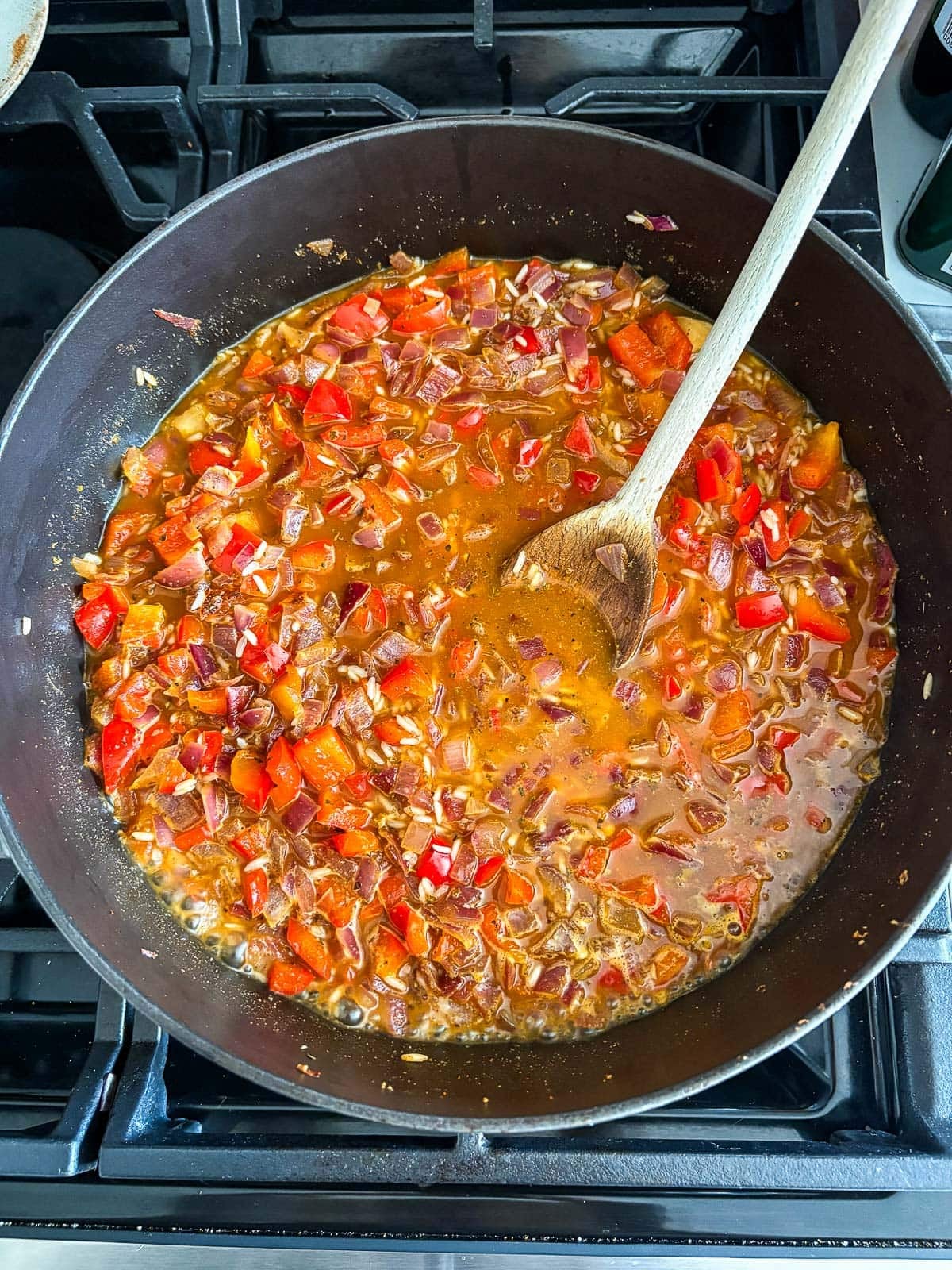 dutch oven with bell pepper and onion, with white rice, broth and wood spoon.