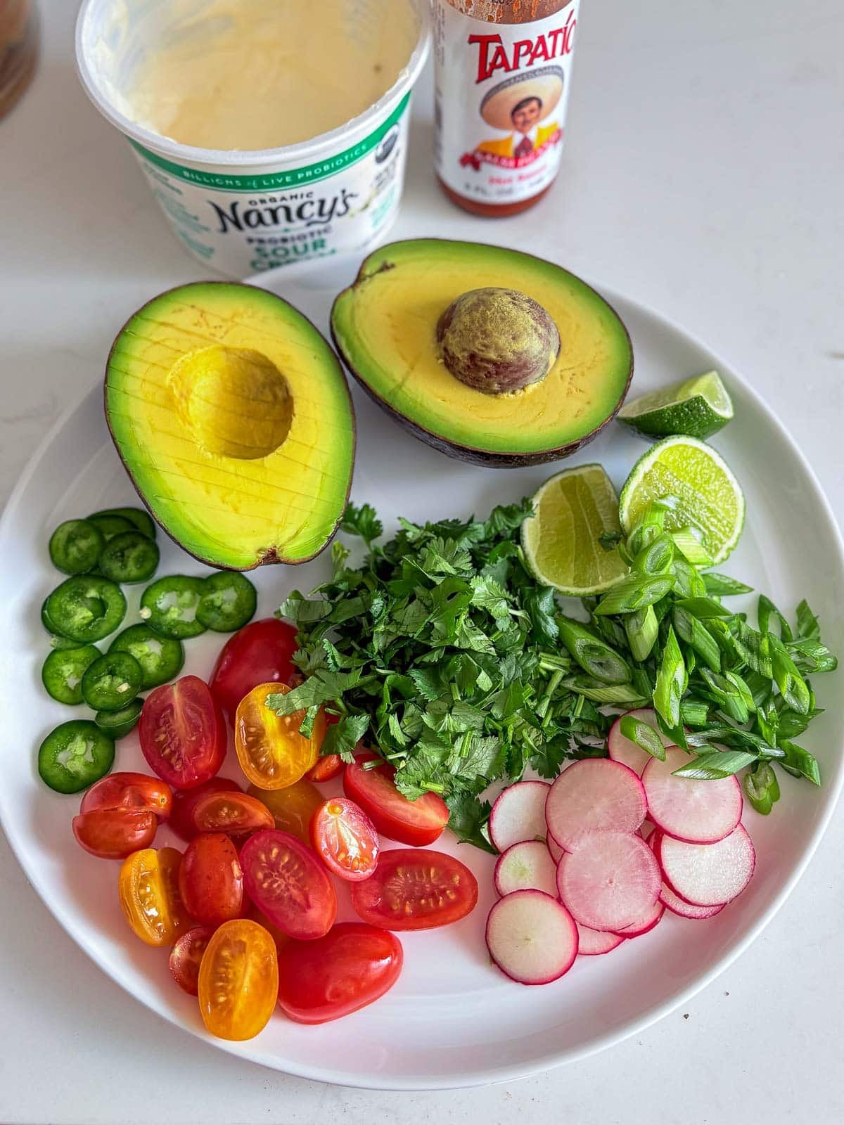 toppings for cheesy rice and beans on plate - avocado halves, sliced jalapeno, cherry tomatoes, sliced radish, fresh herbs, and lime.