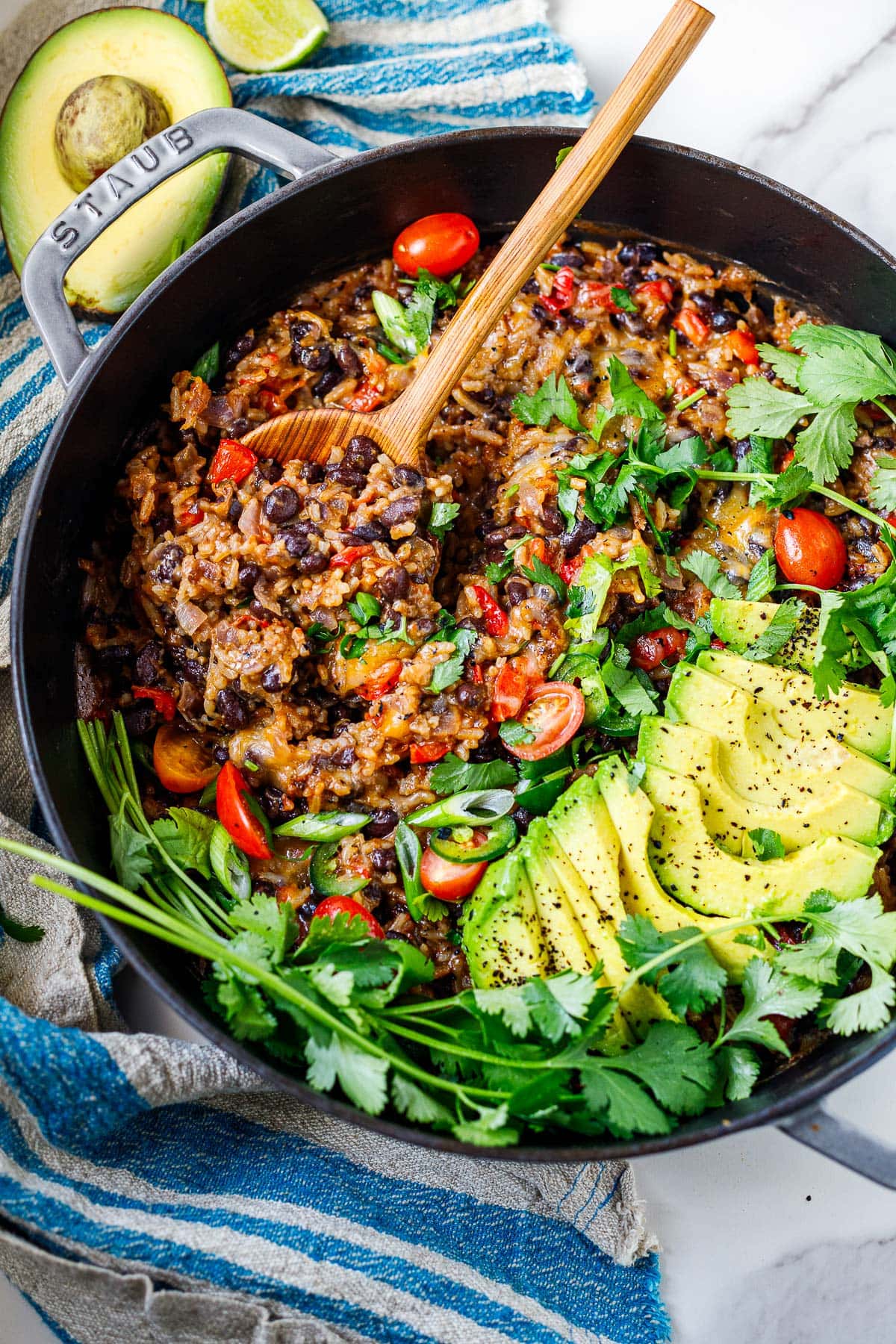 cheesy rice and beans in cast iron skillet with sliced avocado, cherry tomatoes, fresh herbs, and scallions.