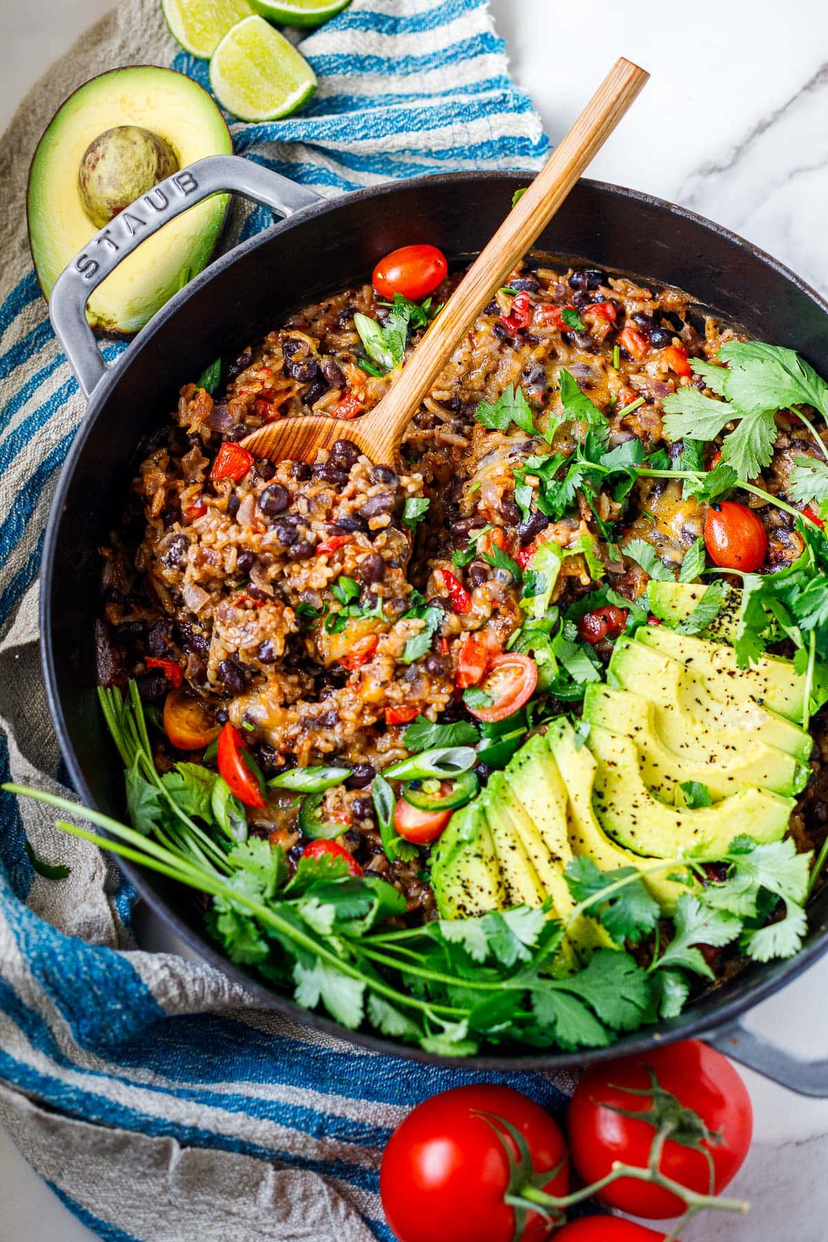 dutch oven with cheesy rice and beans garnished with cherry tomatoes, cilantro, and slived avocado.