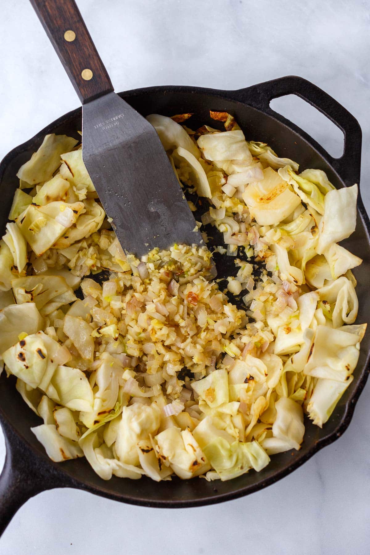 metal spatula stirring aromatics, surrounded by stir-fried green cabbage in cast iron. 