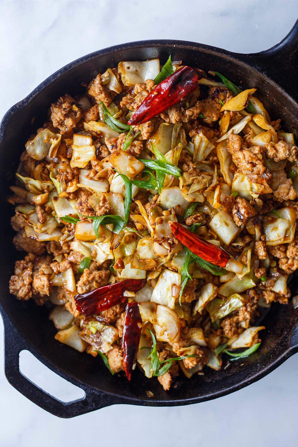 chicken and cabbage stir fry in cast iron skillet with dried red chilies and scallions. 
