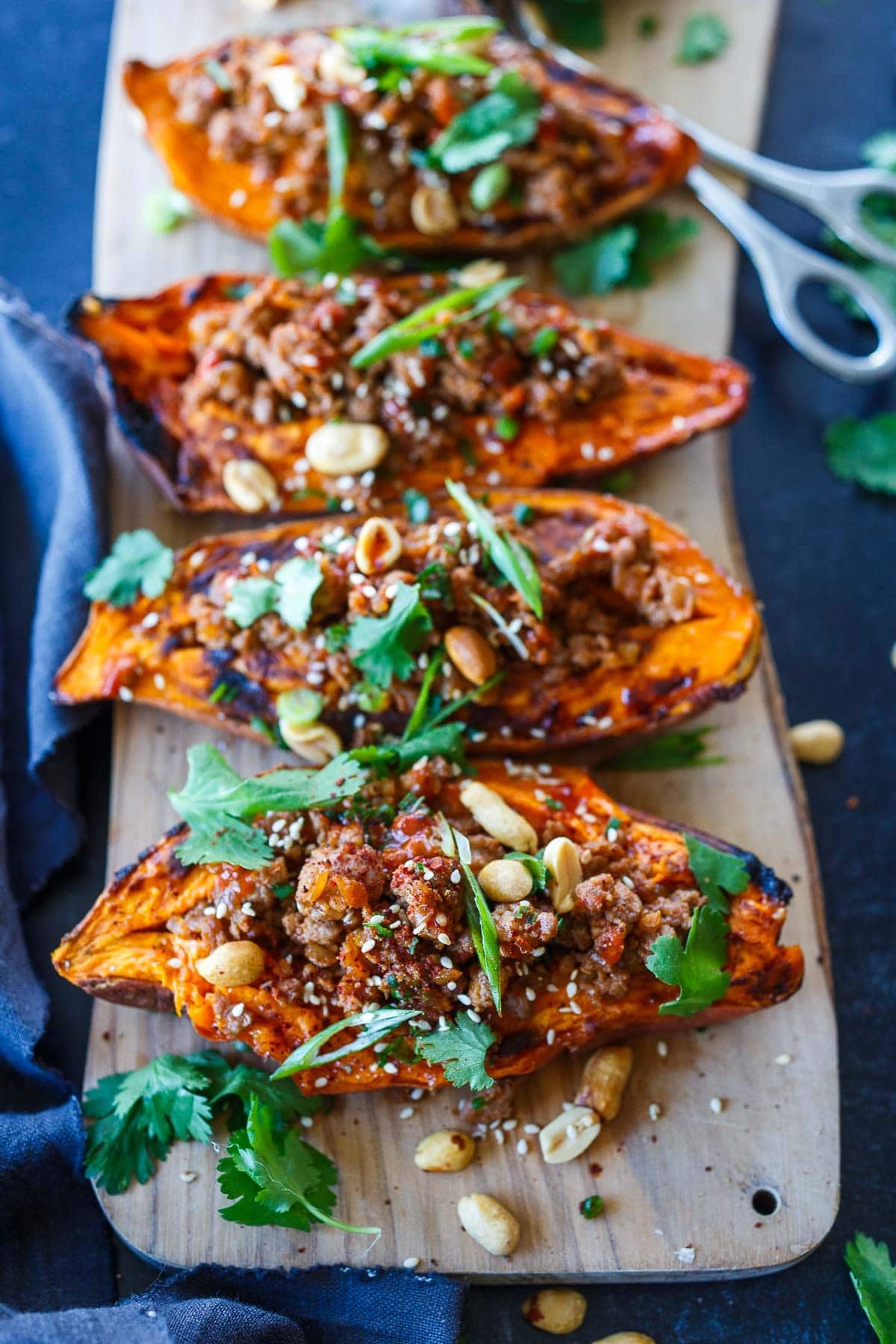 Ground turkey stuffed sweet potatoes on a wood serving board with a garnish of peanuts and fresh herbs.