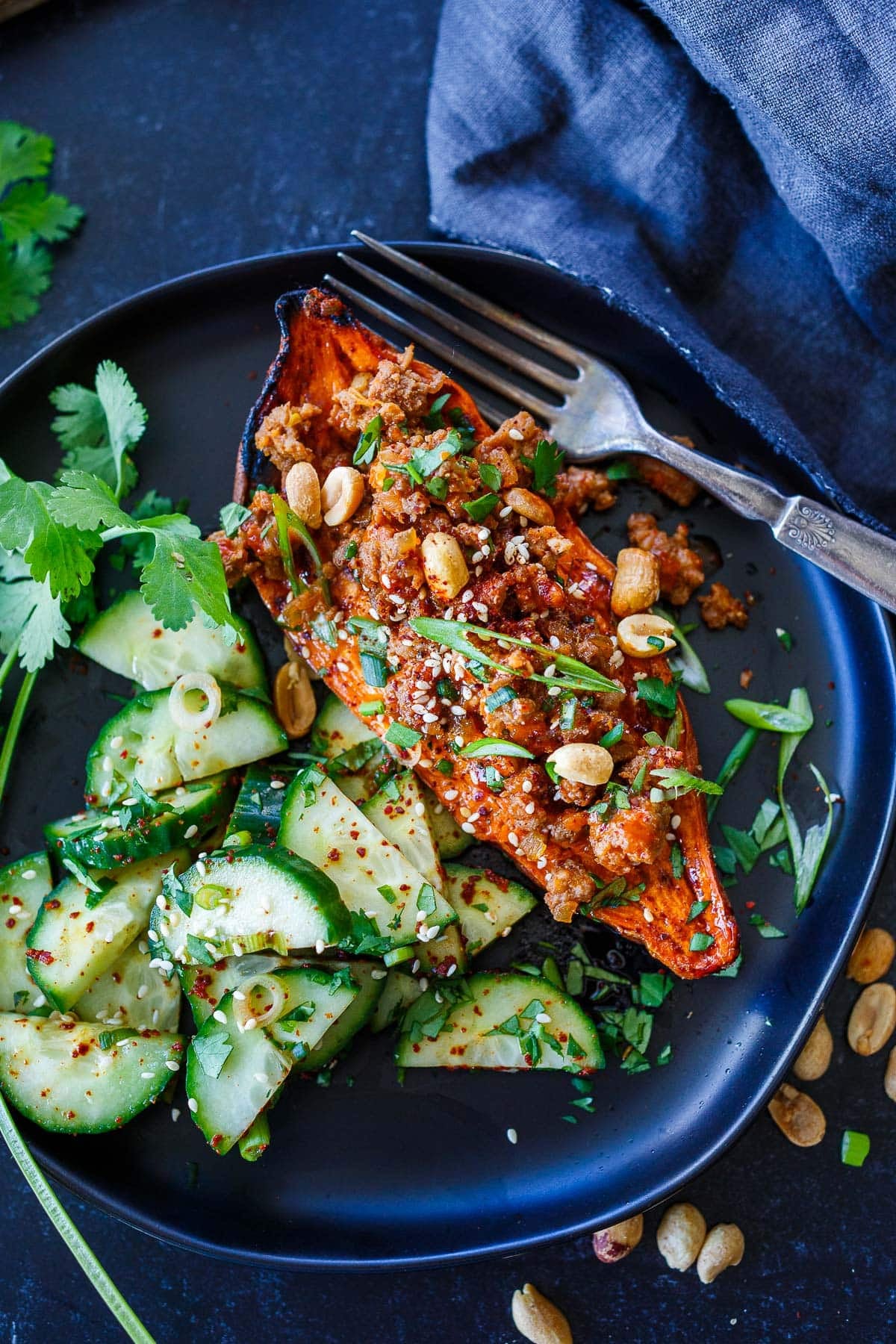 plate with Gochujang sweet potatoes with ground meat and topped with green onions and peanuts with a side of Korean cucumber salad and fresh cilantro.