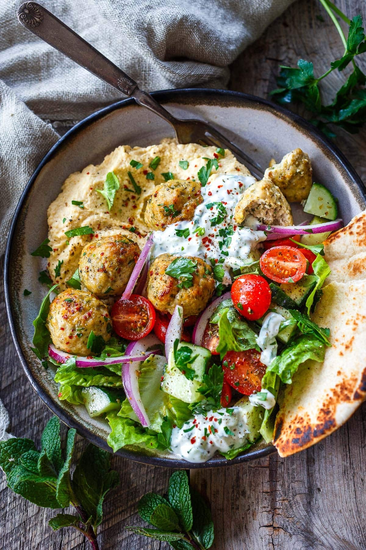 Greek bowl with hummus, tzatziki, Greek chicken meatballs, lettuce, tomato, cucumber, red onion, and pita. 