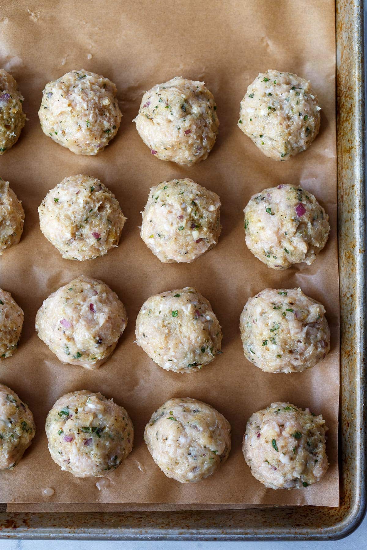 Greek chicken meatballs shaped and placed on parchment-lined baking sheet.