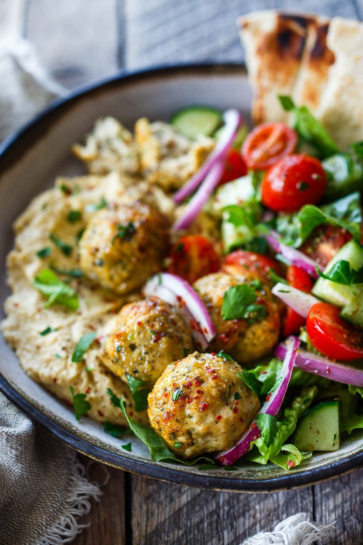 bowl of Greek chicken meatballs on top of hummus with a Greek salad. 