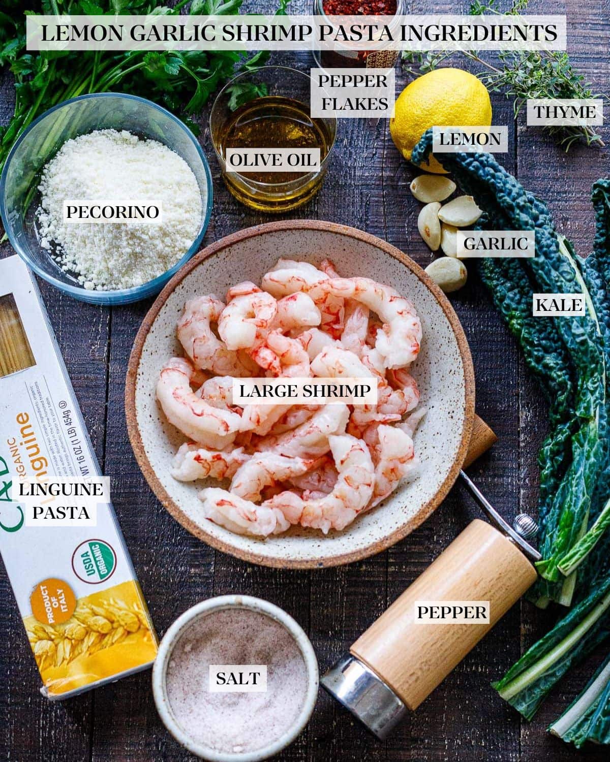 ingredients for shrimp pasta on wood table - bowl of shrimp, lacinato kale, garlic cloves, oil, lemon pecorino, aleppo, salt, linguine