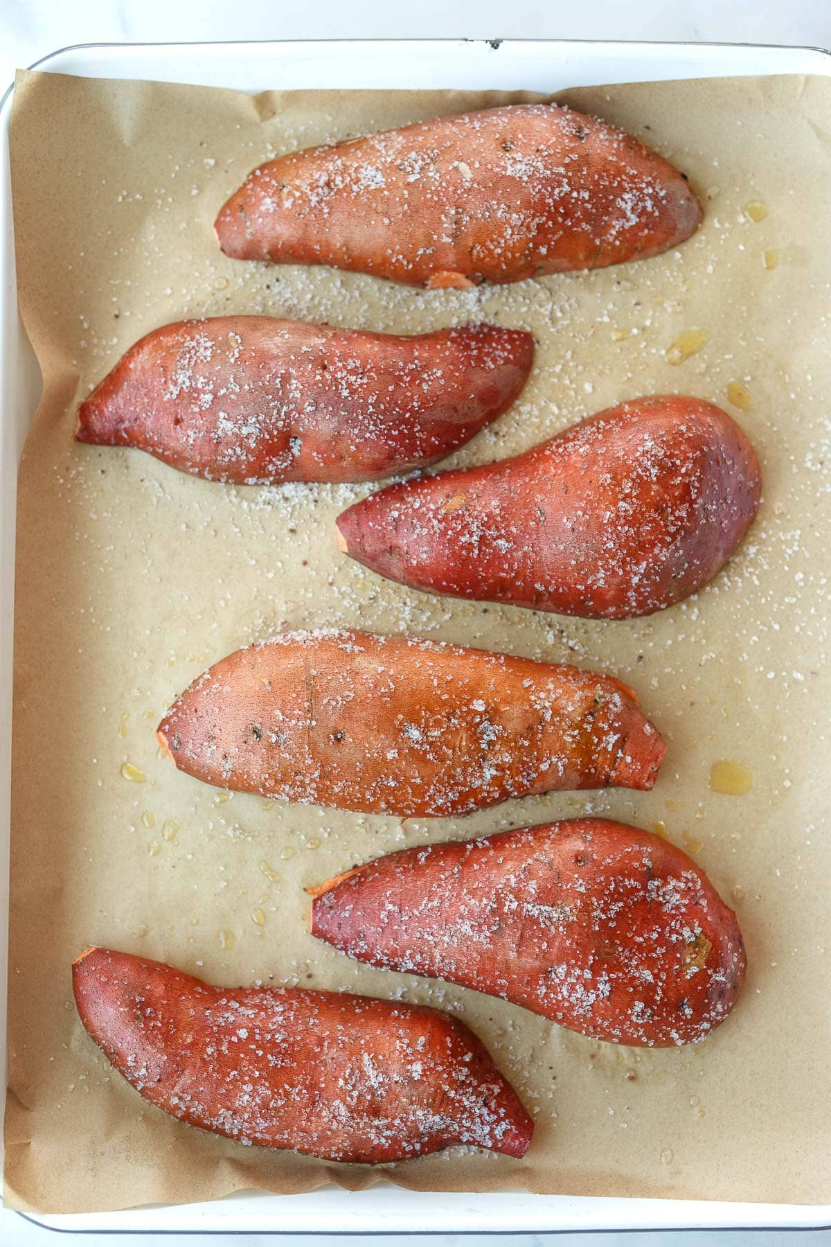 sweet potato halves cut side down on parchment lined baking sheet with salt rub.
