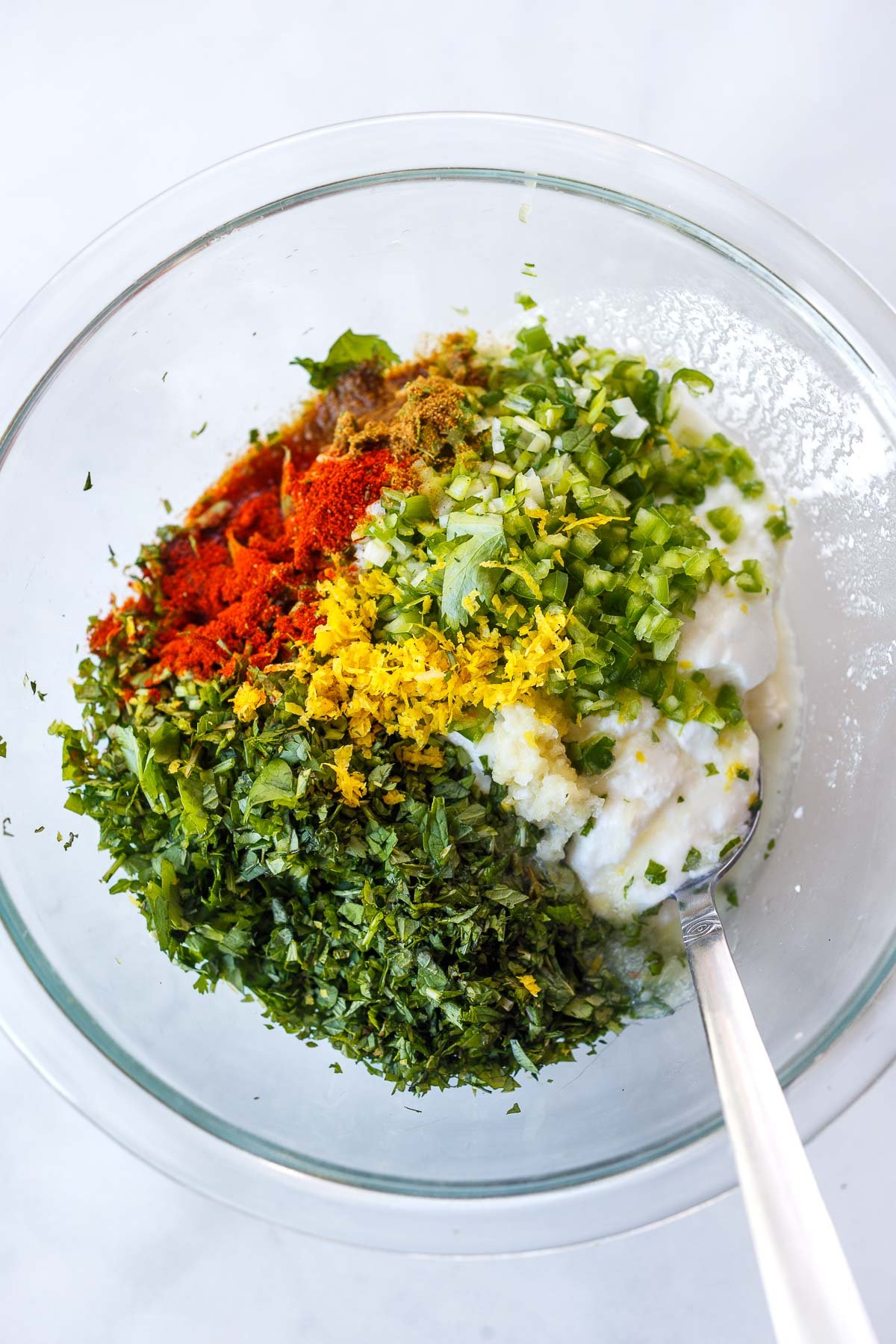 glass mixing bowl with yogurt, fresh herbs, serrano chili, lemon zest, and spices.