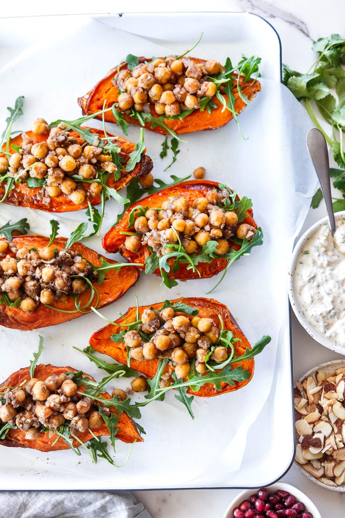 stuffed sweet potatoes with Moroccan chickpeas and arugula on serving platter next to toppings.