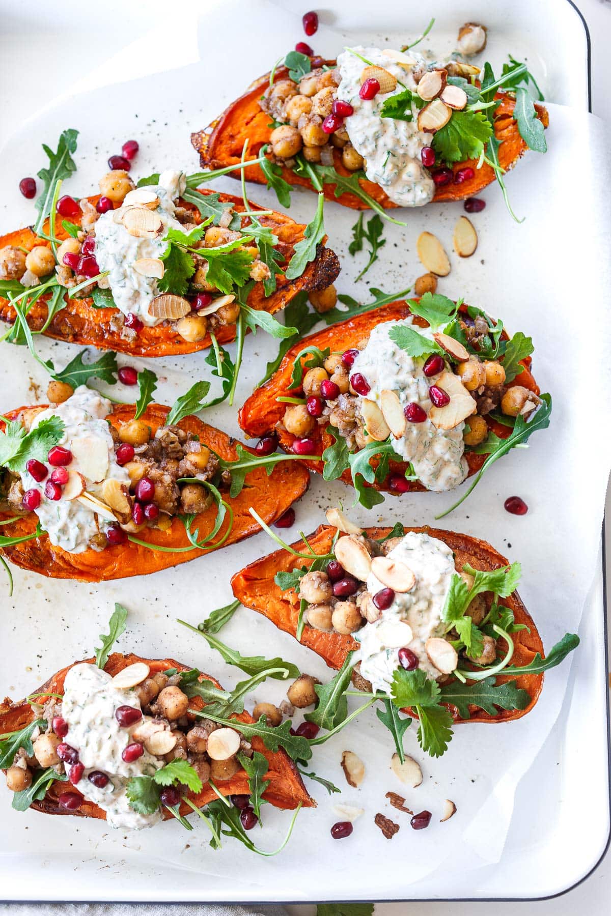 serving platter with stuffed sweet potatoes with Moroccan chickpeas, arugula, herby yogurt, sliced almonds, and pomegranate seeds.