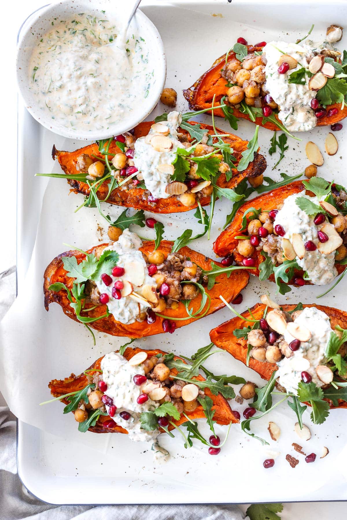 serving tray with stuffed sweet potatoes with Moroccan chickpeas, arugula, herbed yogurt sauce, sliced almonds, pomegranate seeds and cilantro.