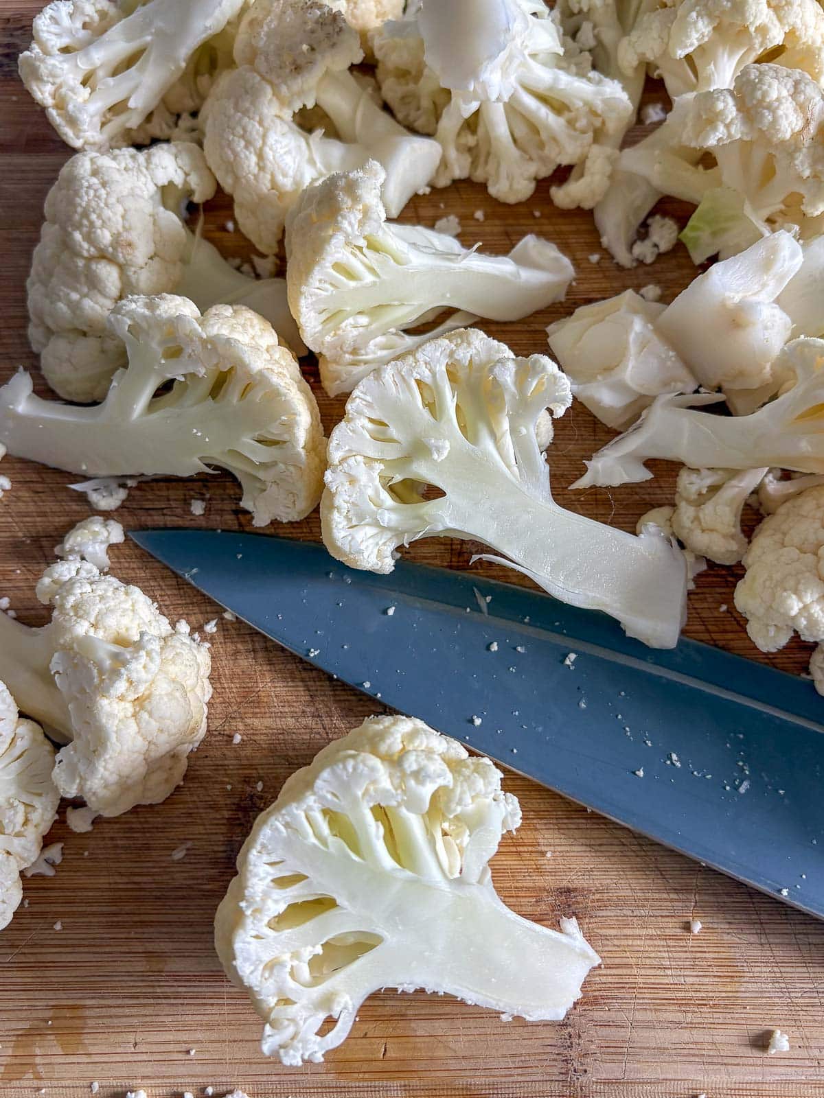 sharp knife and cauliflower florets on wood board.