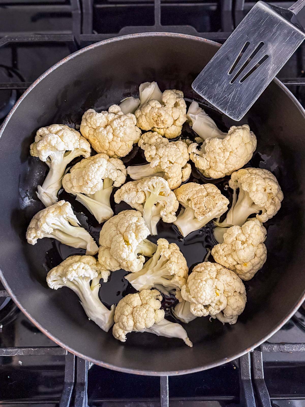 metal spatula leaning against skillet with cauliflower florets searing.