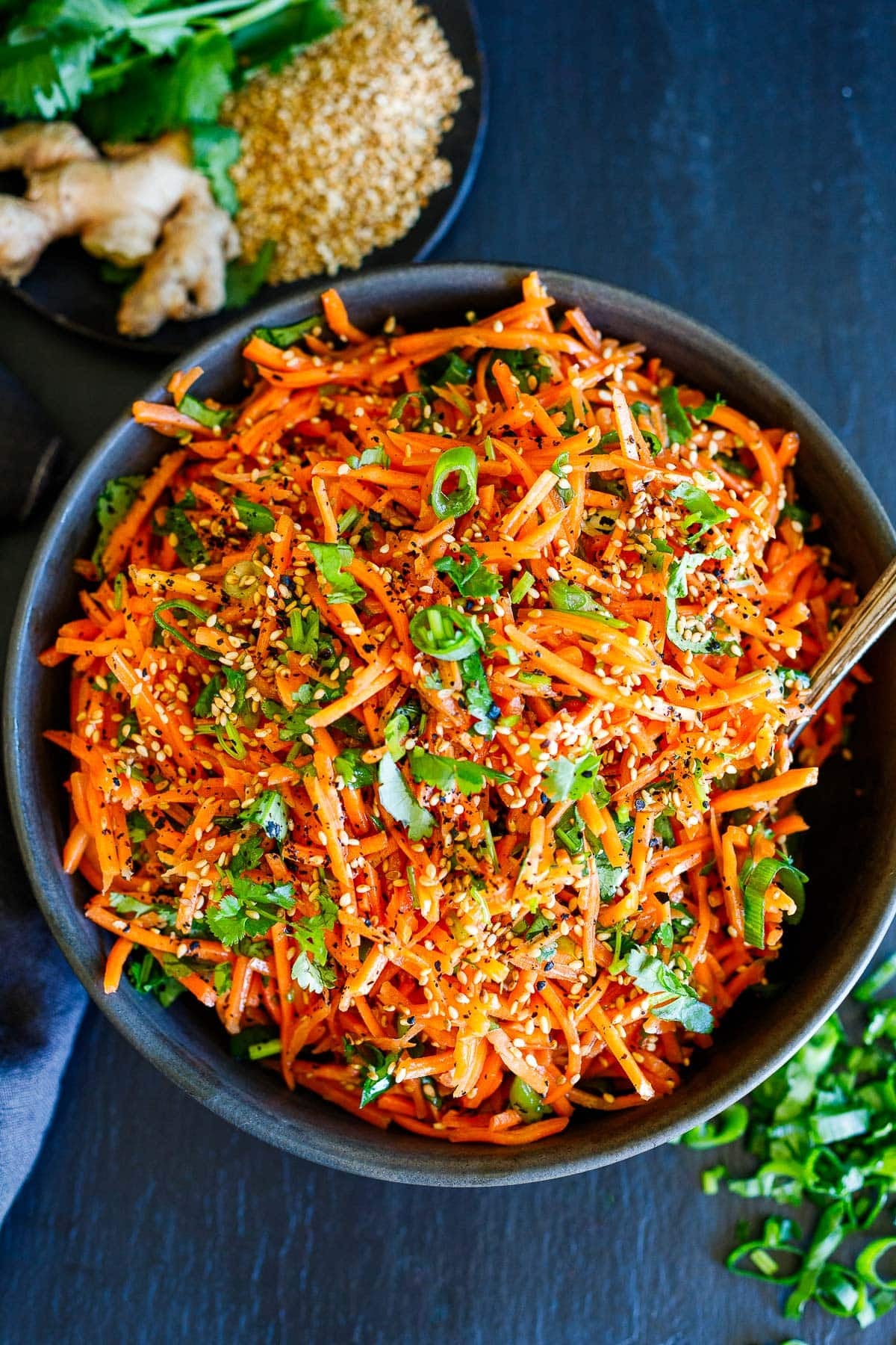 Asian carrot salad in bowl with green onions, cilantro, and sesame seeds.