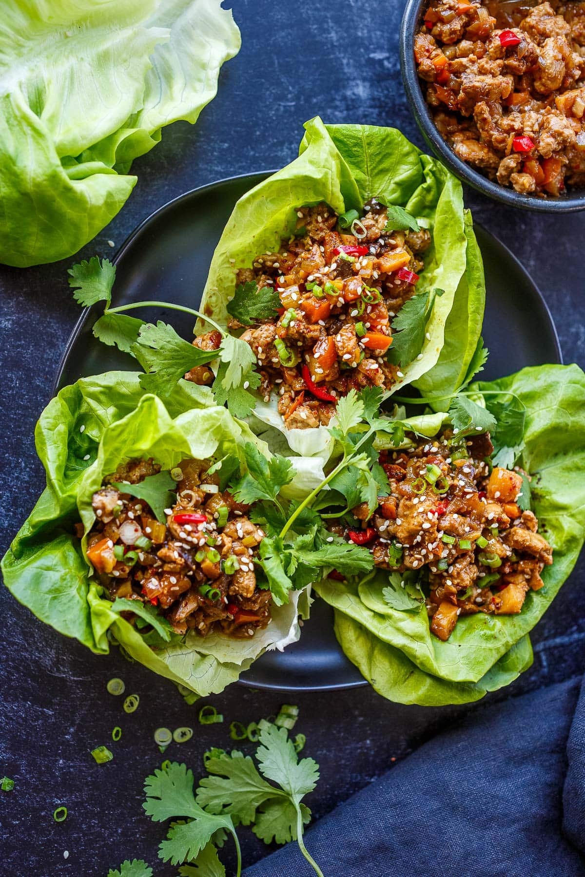 plate of three Asian lettuce wraps with ground meat and veggie filling with green onions, sesame seeds, and fresh cilantro. 