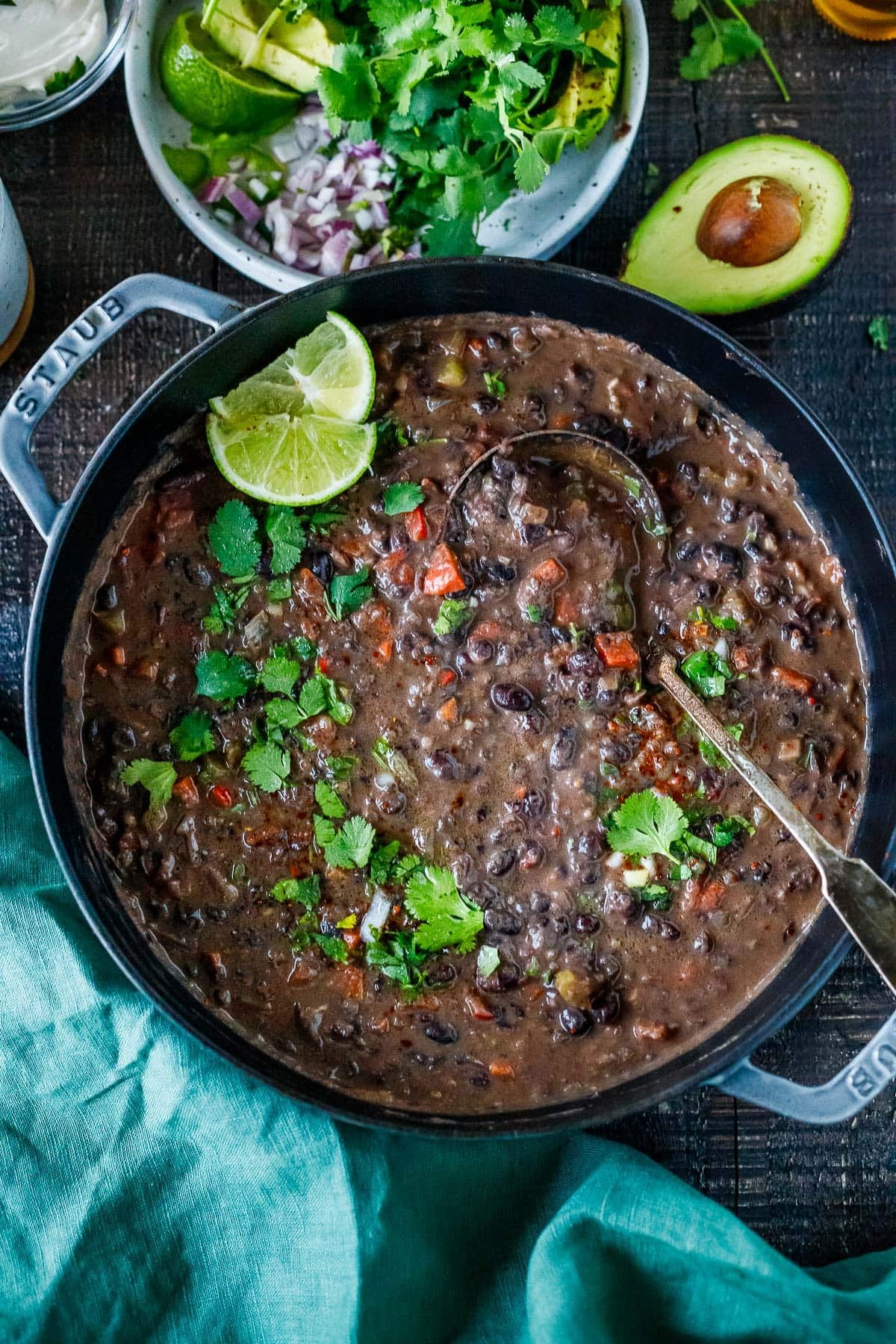 Dutch oven with black bean soup with fresh cilantro and lime wedges and ladle. 