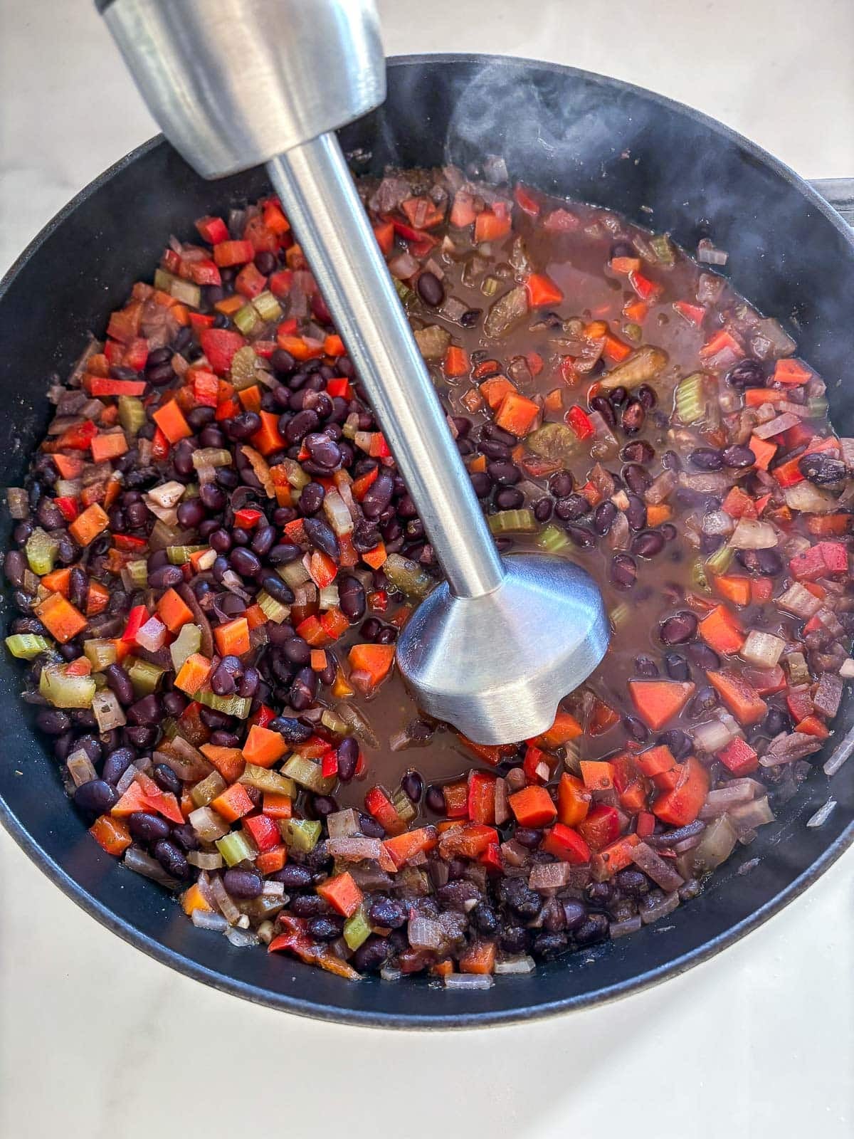 using immersion blender to partially blend black bean soup in pot. 