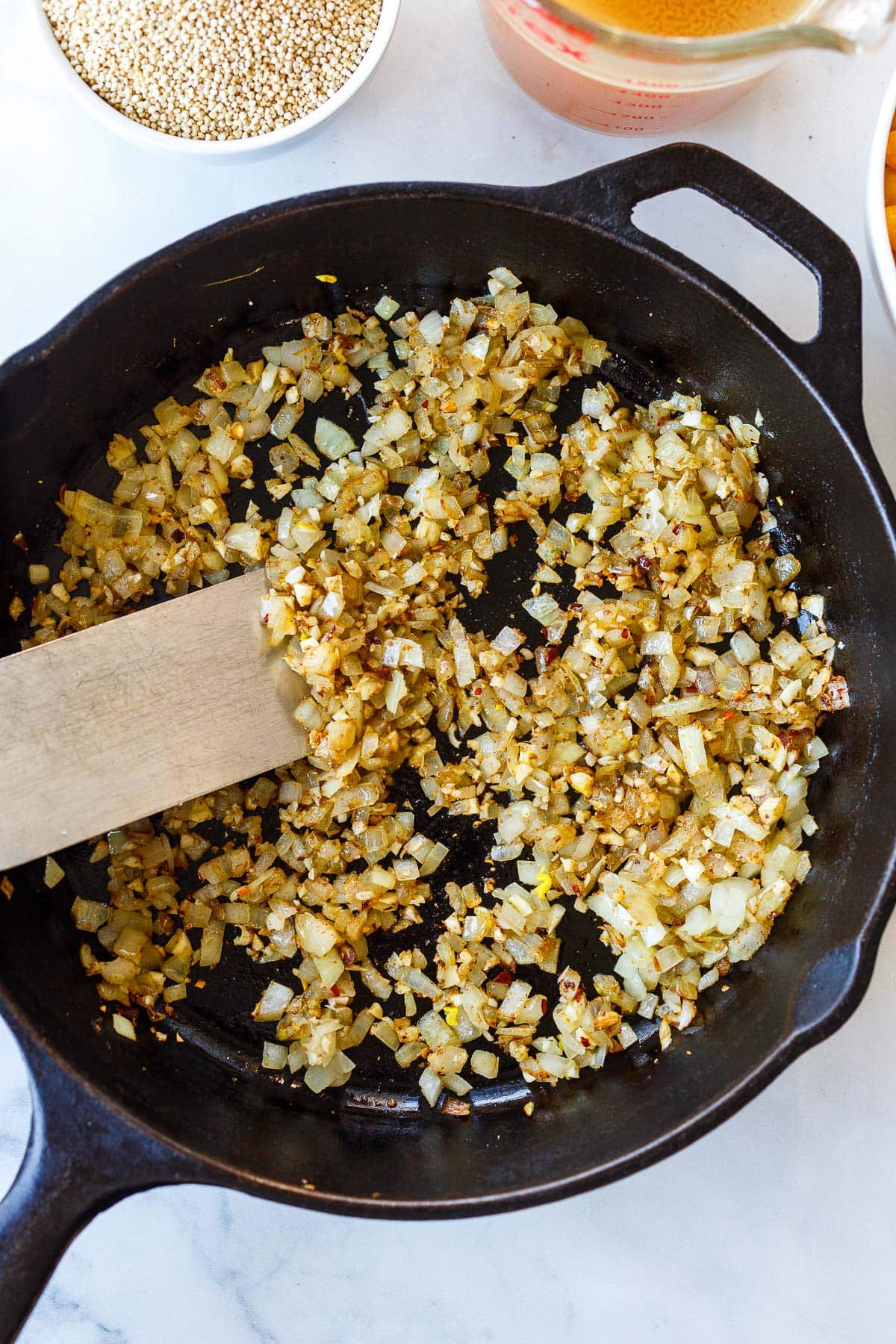 cast iron skillet with sautéed onions and garlic with metal spatula. 