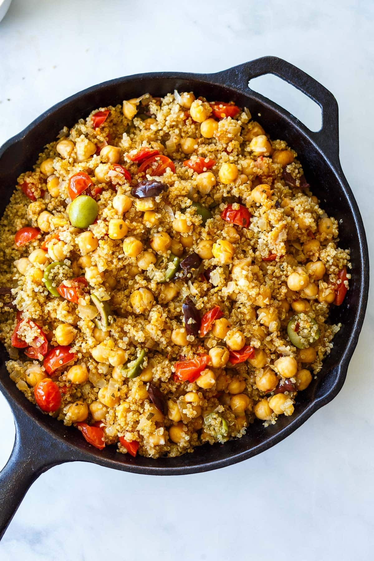 cast iron skillet with cooked Mediterranean chickpea skillet with olives and tomatoes. 
