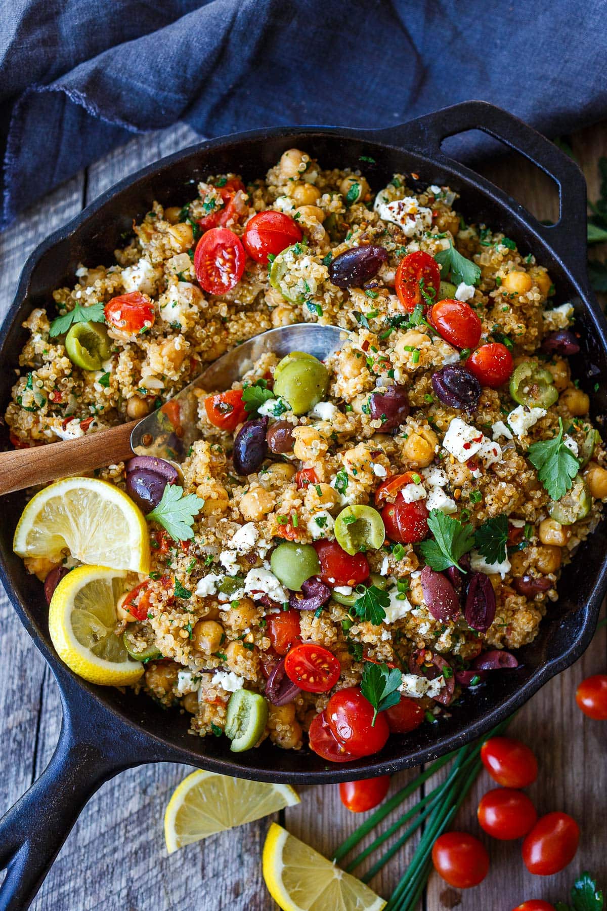 Mediterranean skillet with chickpeas and quinoa, tomatoes, olives, feta, herbs, and lemon wedges. 