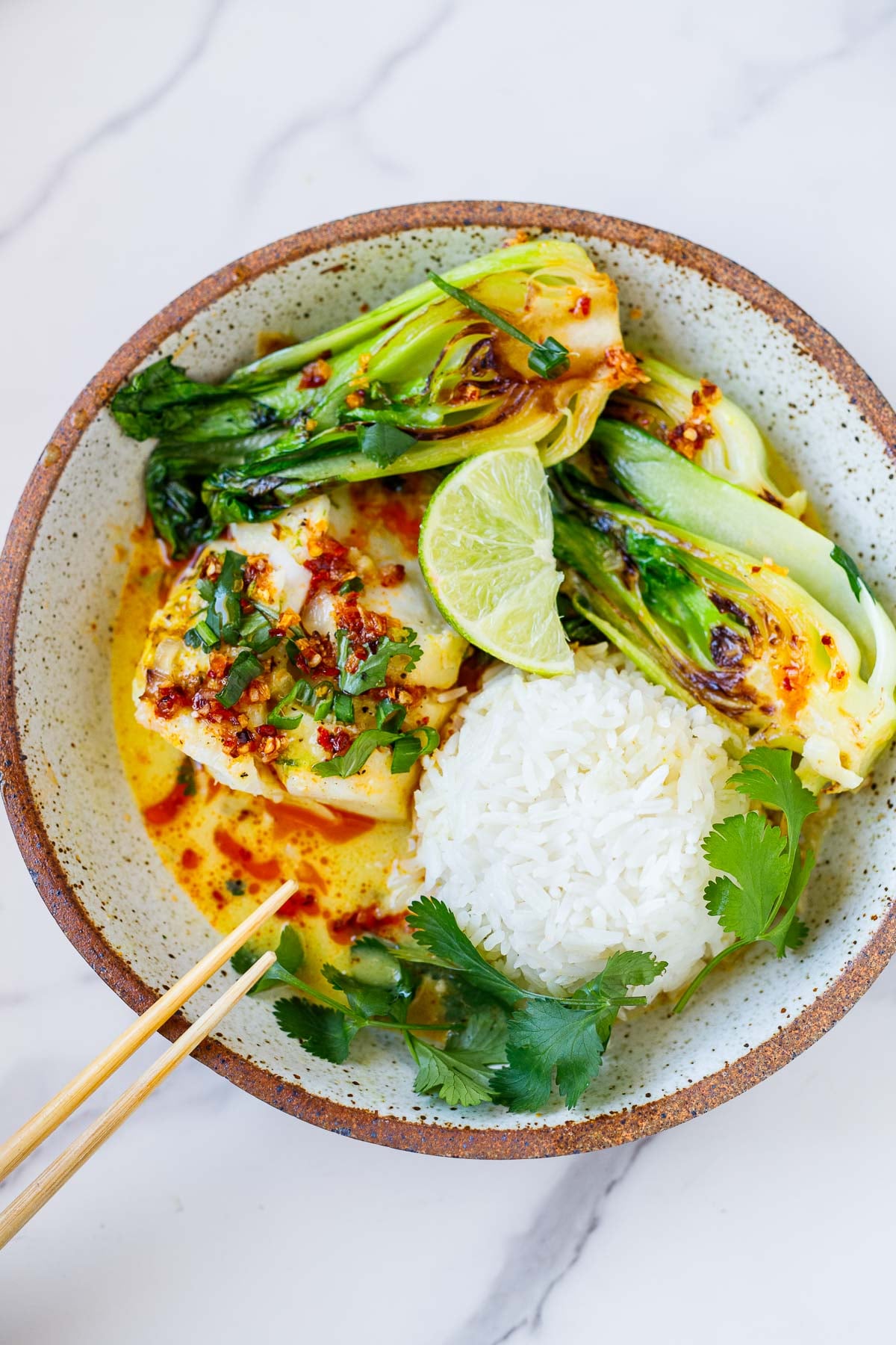 cod recipe in bowl of coconut broth with jasmine rice, seared bok choy, lime wedge, cilantro, scallions, and chili crisp.