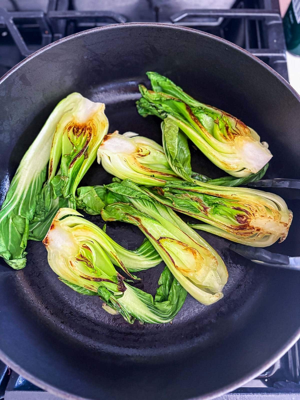 tongs flipping bok choy to reveal seared side in braiser.