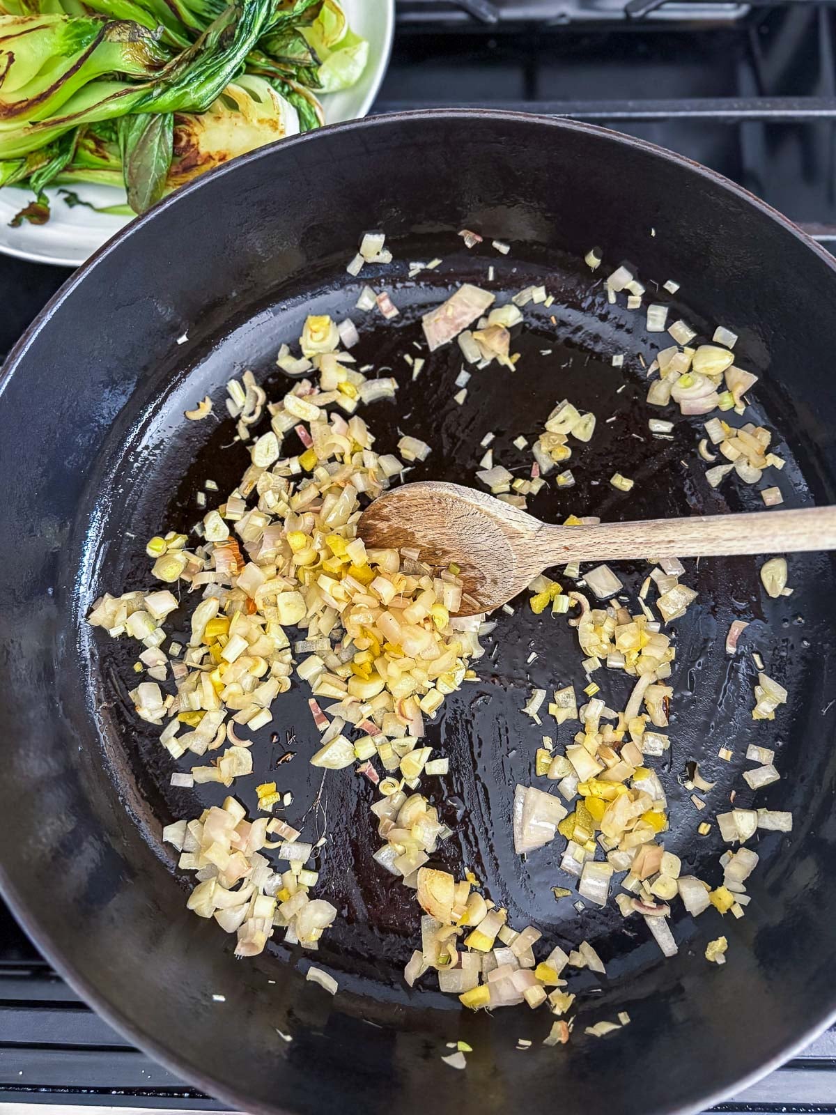 wood spoon sautéing garlic, ginger, and shallots in large pot.