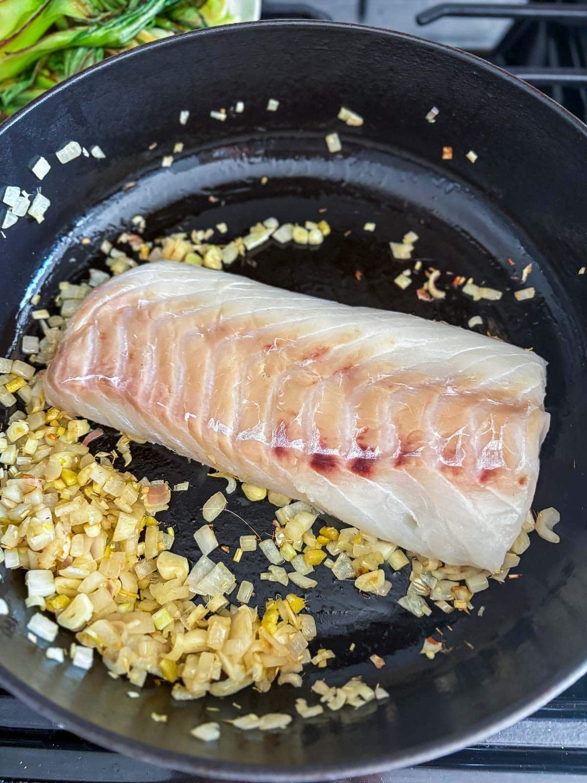 seared cod in pot with sautéed aromatics.