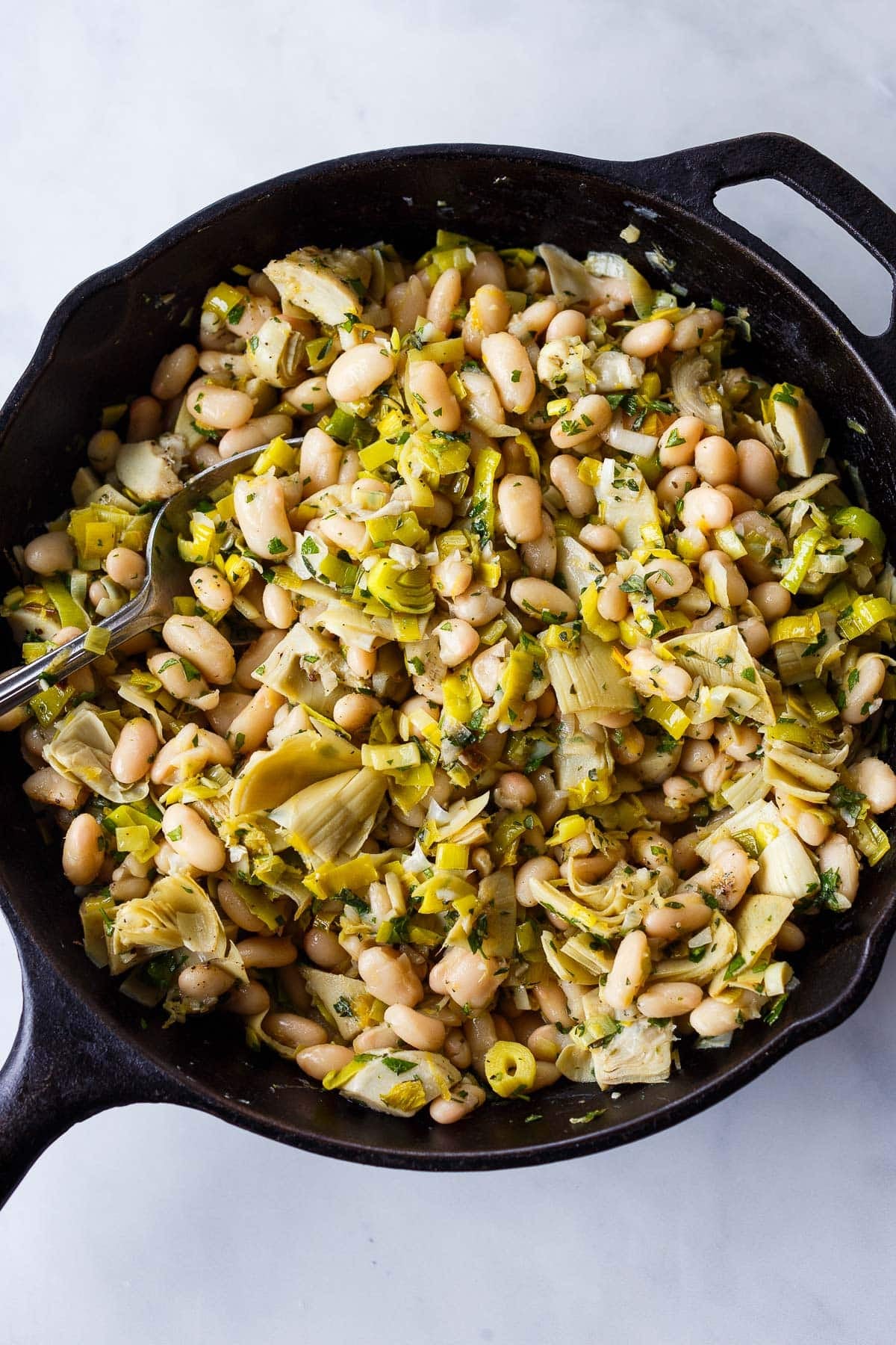cast iron skillet with white beans, artichokes, leeks, and herbs.