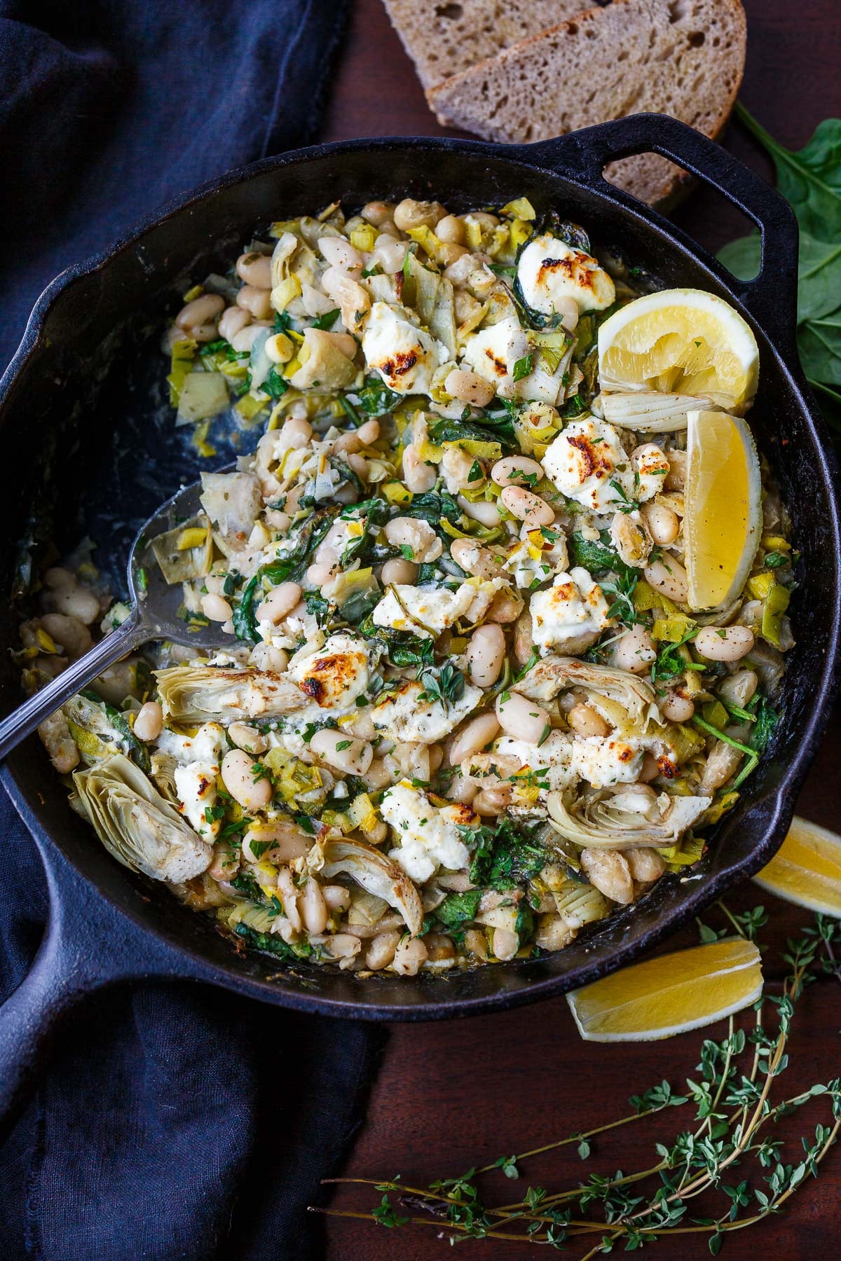 cast iron skillet with white beans, artichokes, leeks, broiled goat cheese, lemon wedges, and fresh herbs.