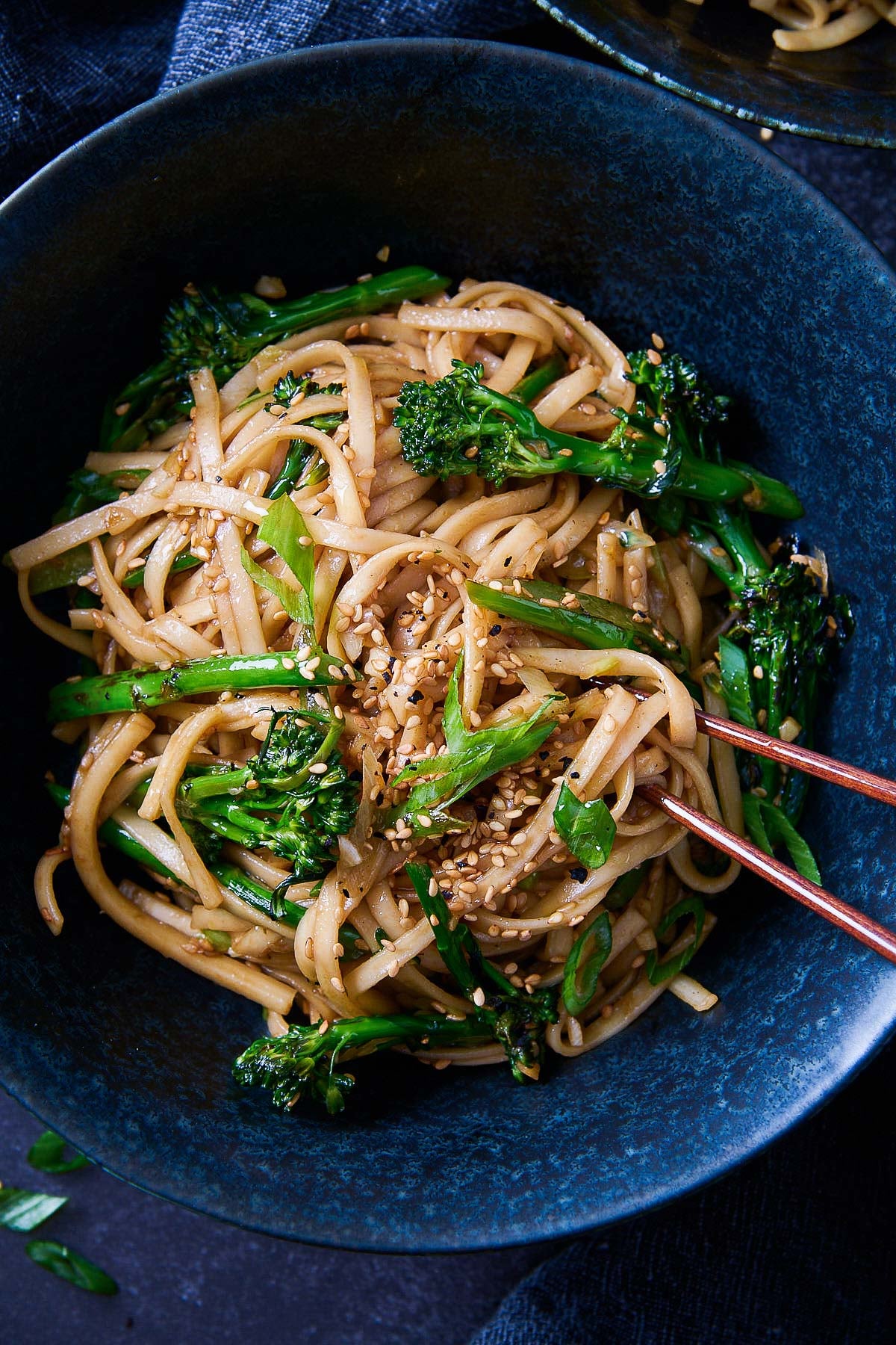 bowl of garlic noodles with broccolini and scallions with sesame seeds, with chopsticks. 