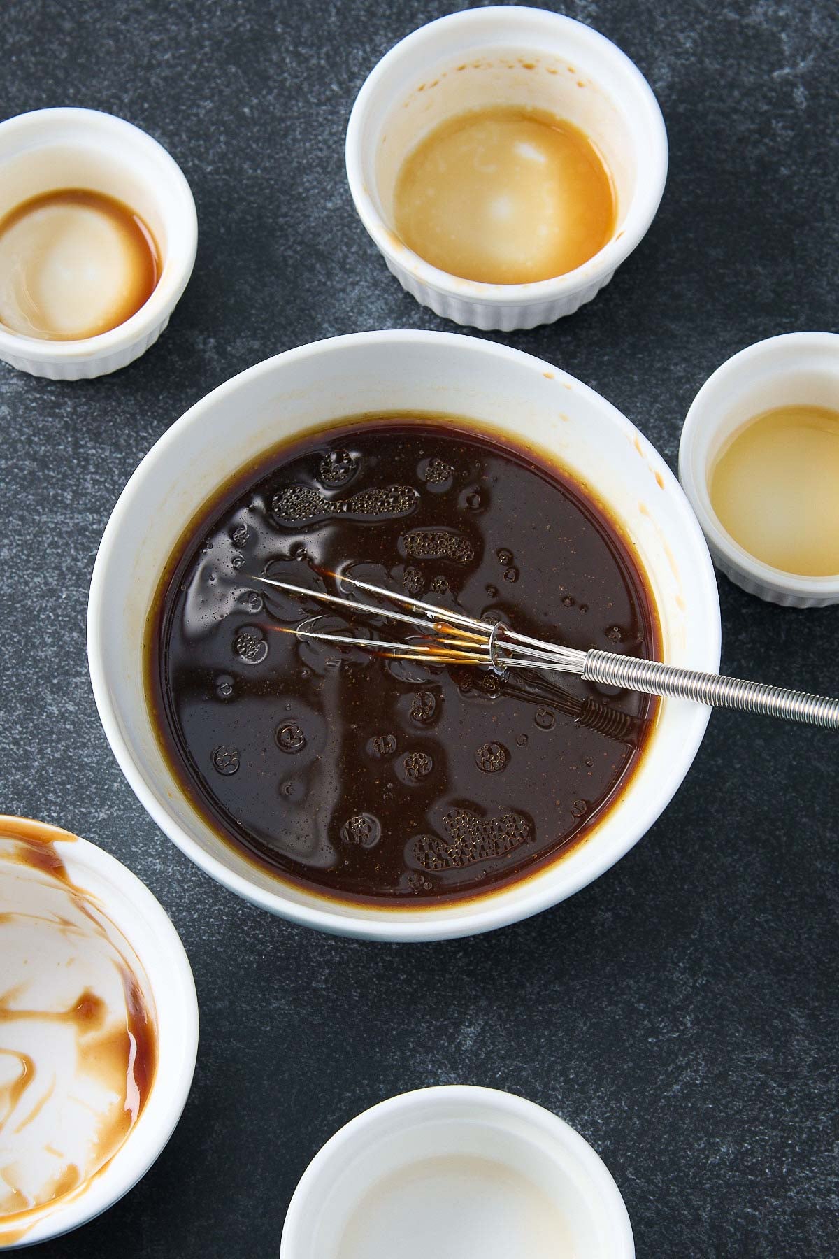 medium mixing bowl with small whisk with hoisin stir fry sauce surrounded by small empty bowls. 