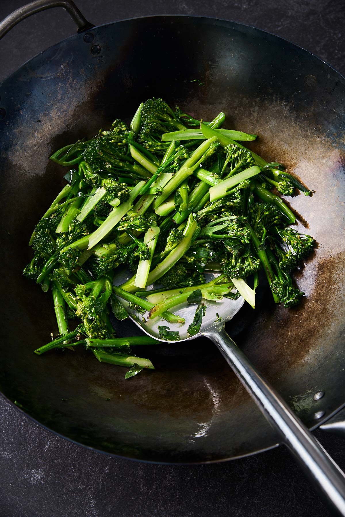 metal spatula stirring broccolini in large wok. 