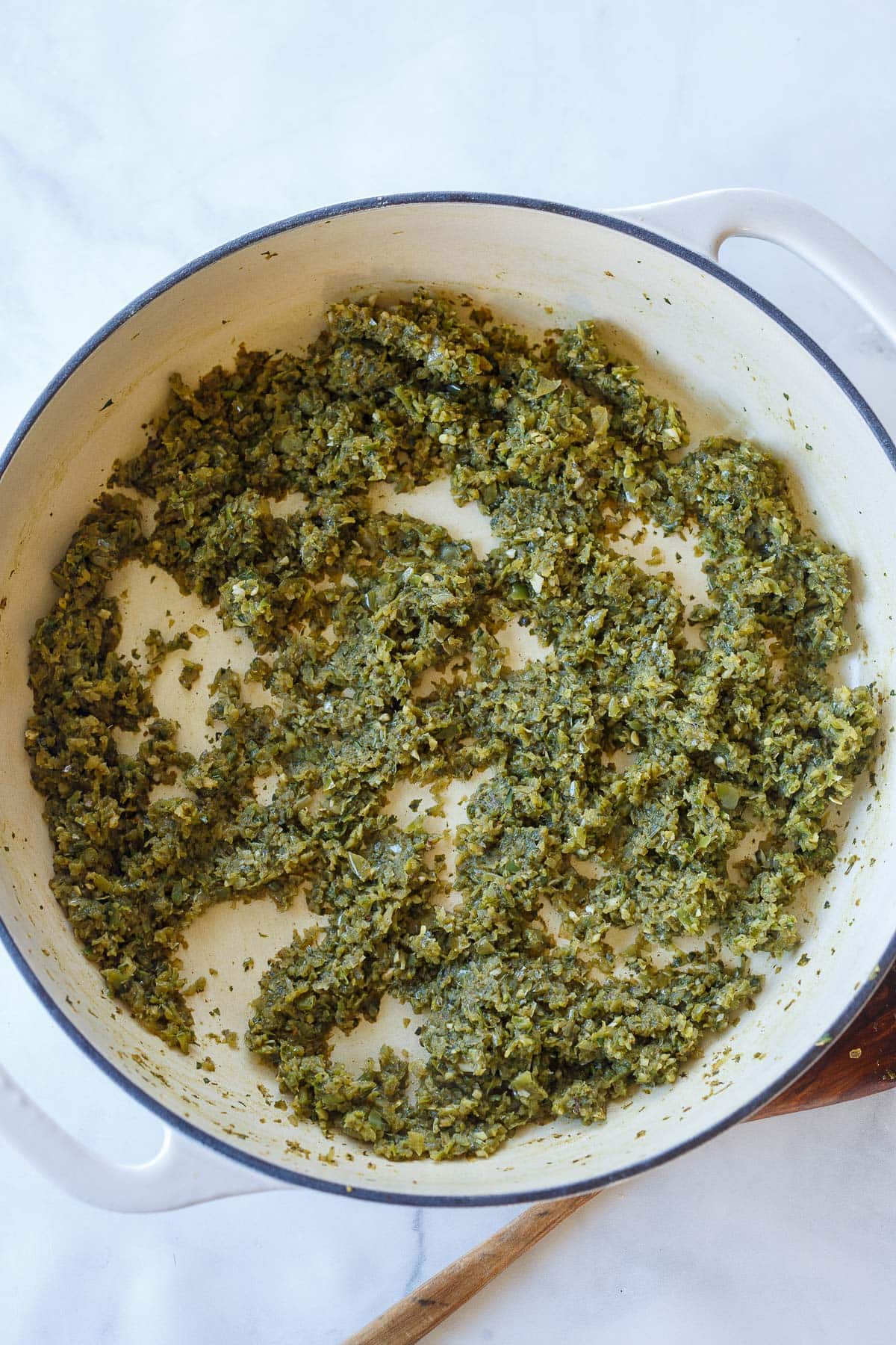 Dutch oven with green veggie herb paste spread across the bottom. 