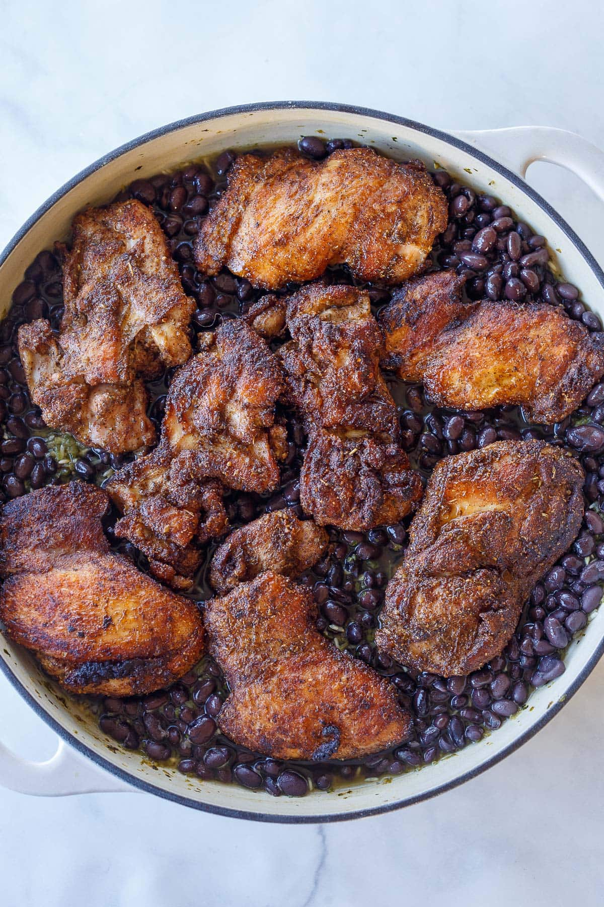 seared Mexican chicken on bed of black beans in a braiser. 