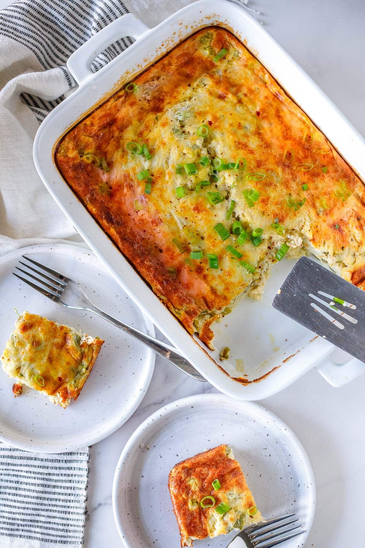 baking dish with breakfast casserole, with two pieces cut out and placed on small plates with forks. 