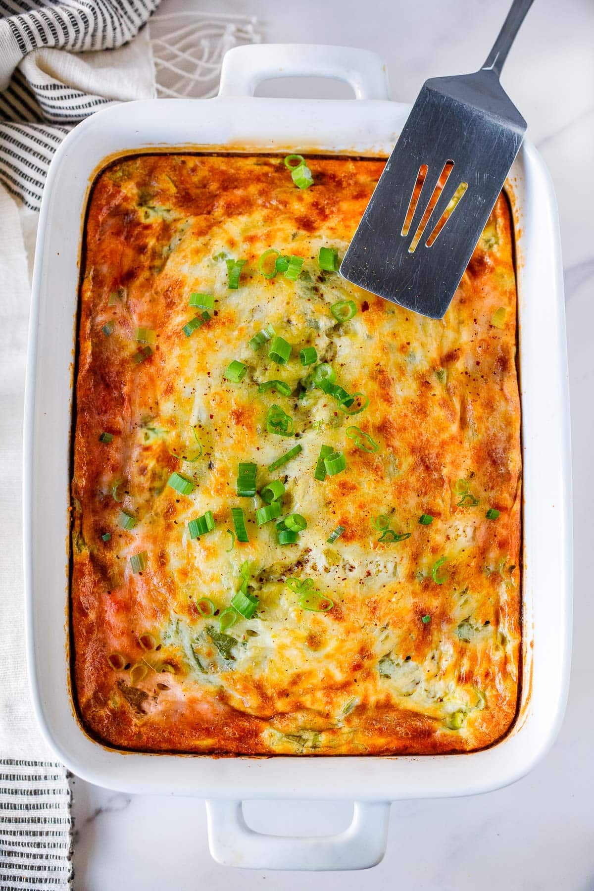 baked breakfast casserole with green chiles in a casserole dish and topped with sliced green onions. 