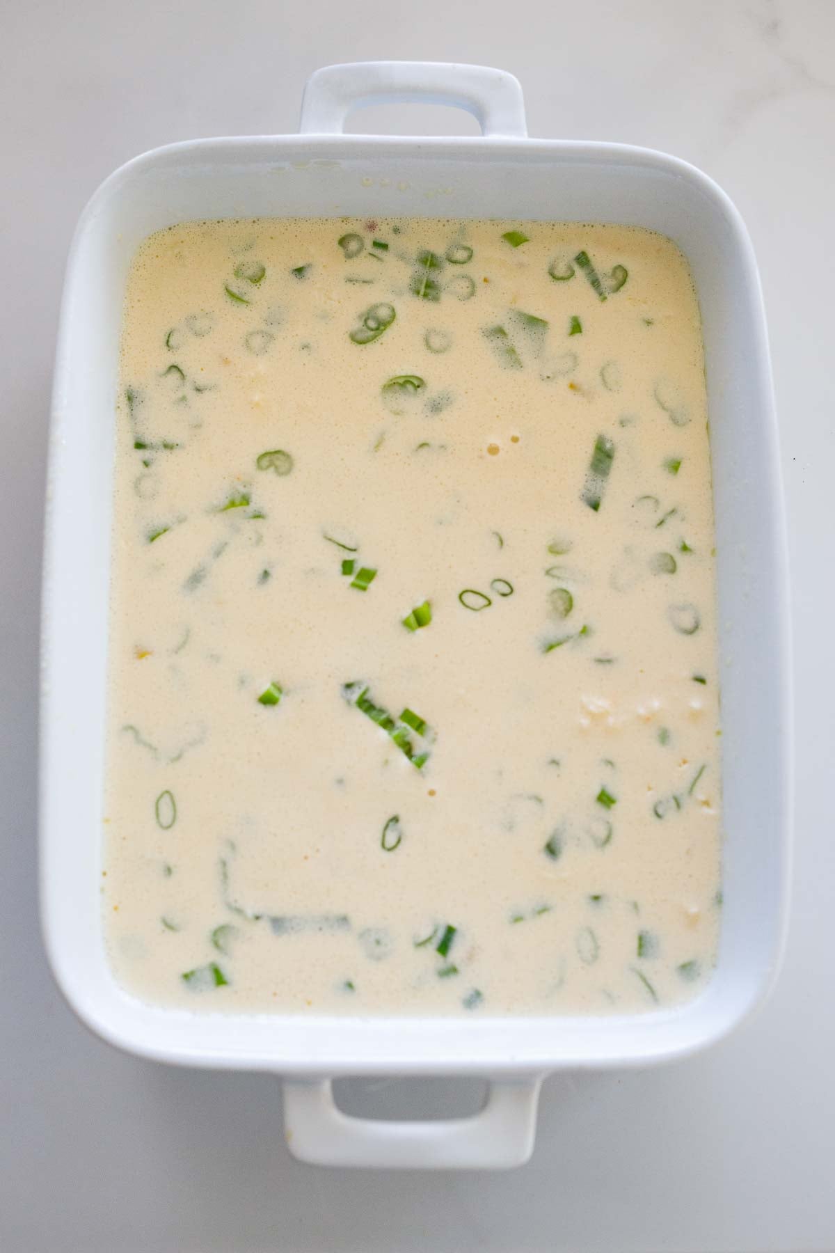 rectangular casserole dish with egg mixture with green onions, unbaked. 