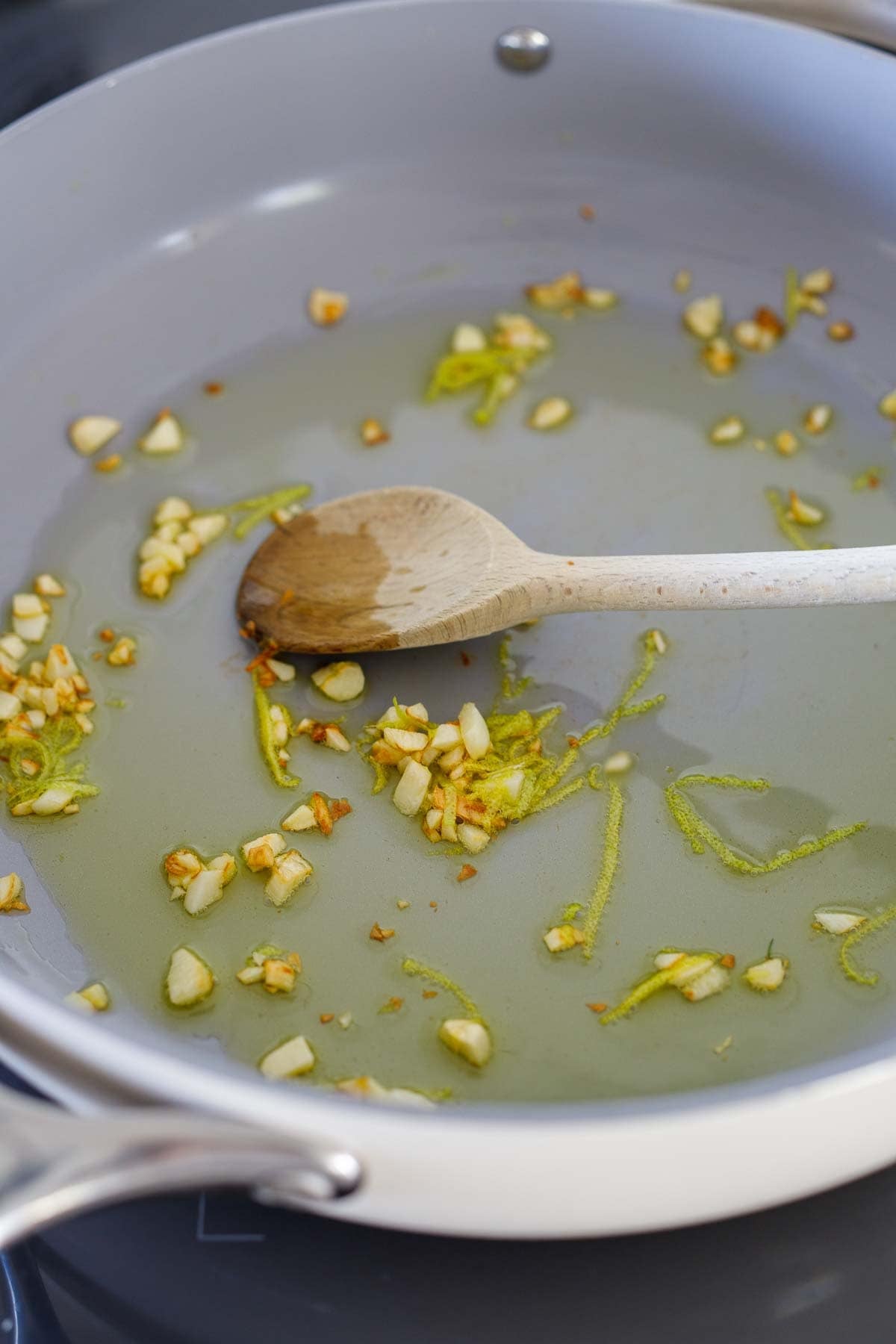 large sauté pan with olive oil, garlic, and lemon zest with wood spoon. 