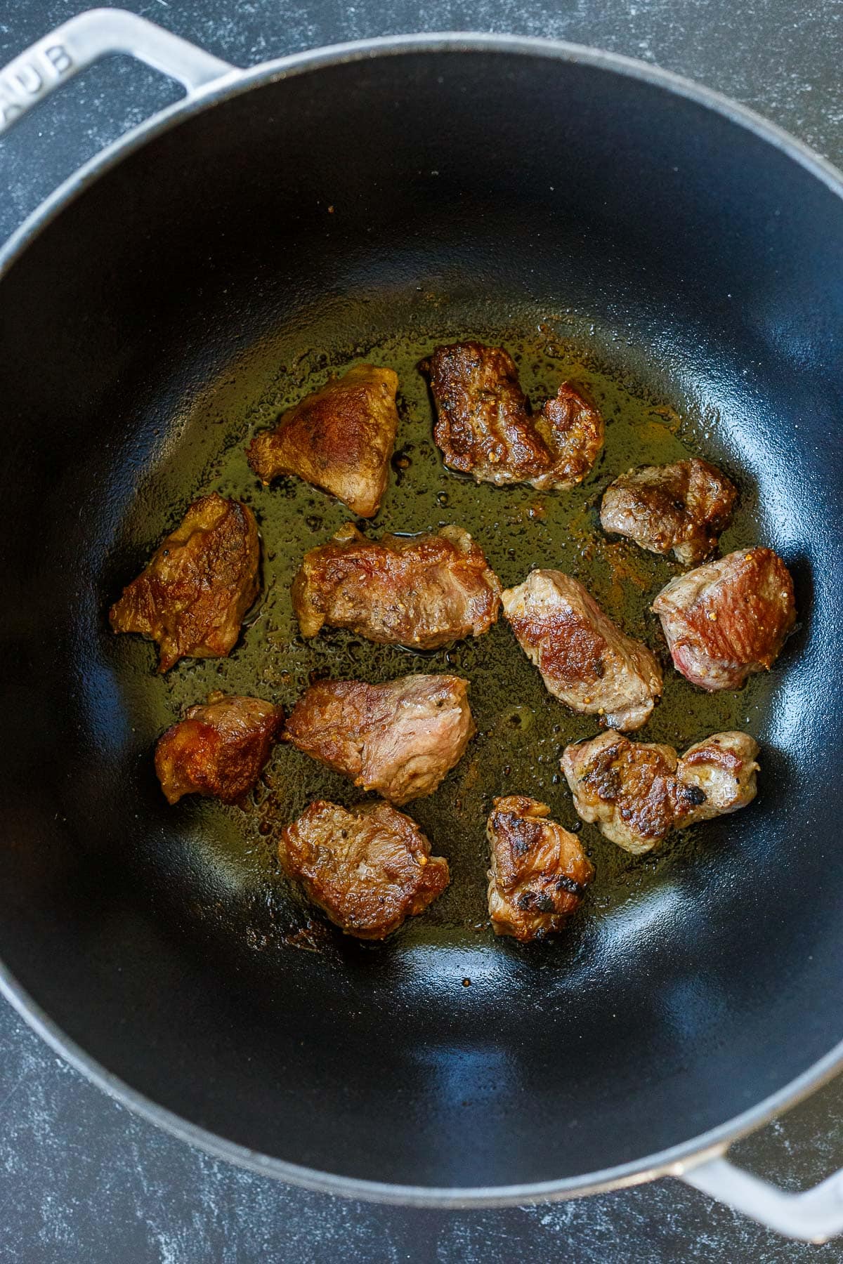 Dutch oven with browned lamb shoulder pieces searing.