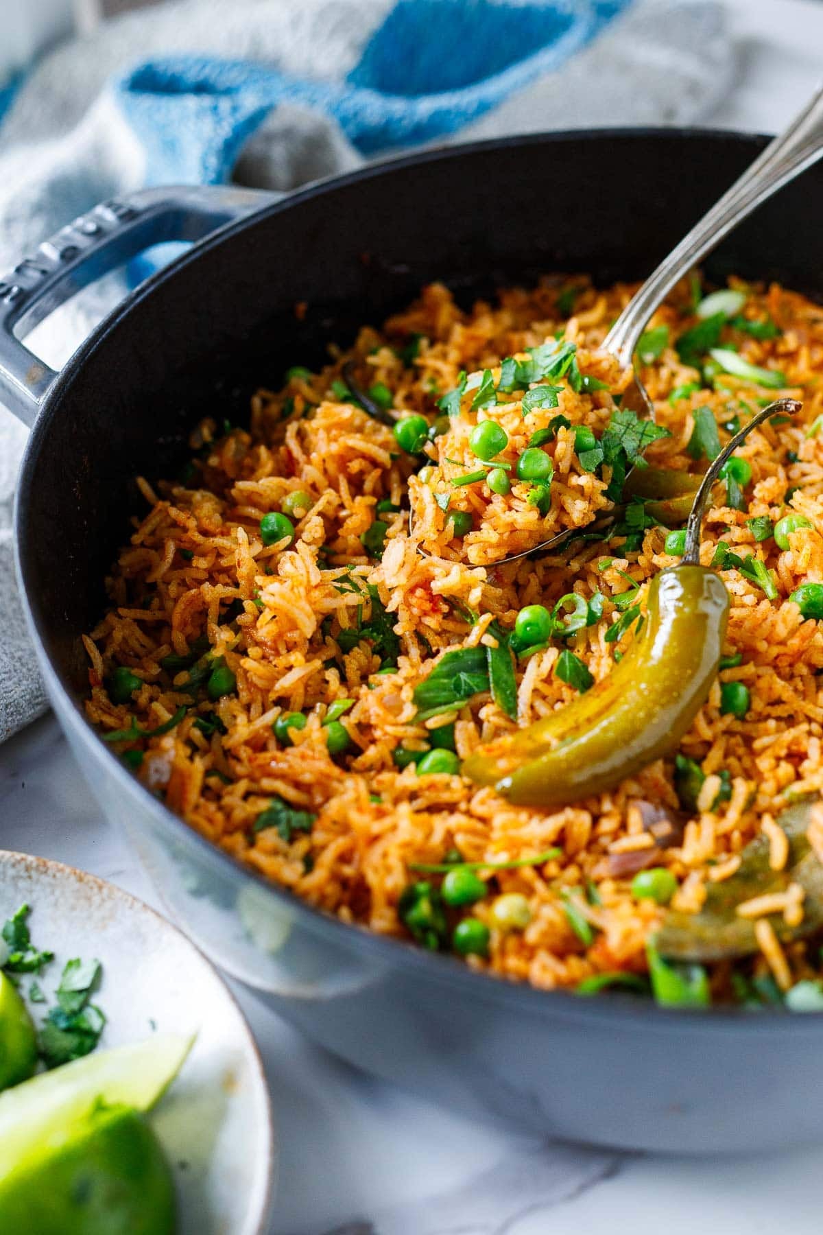 spoon lifting Spanish rice out of the pan with peas and fresh herbs and serrano pepper.