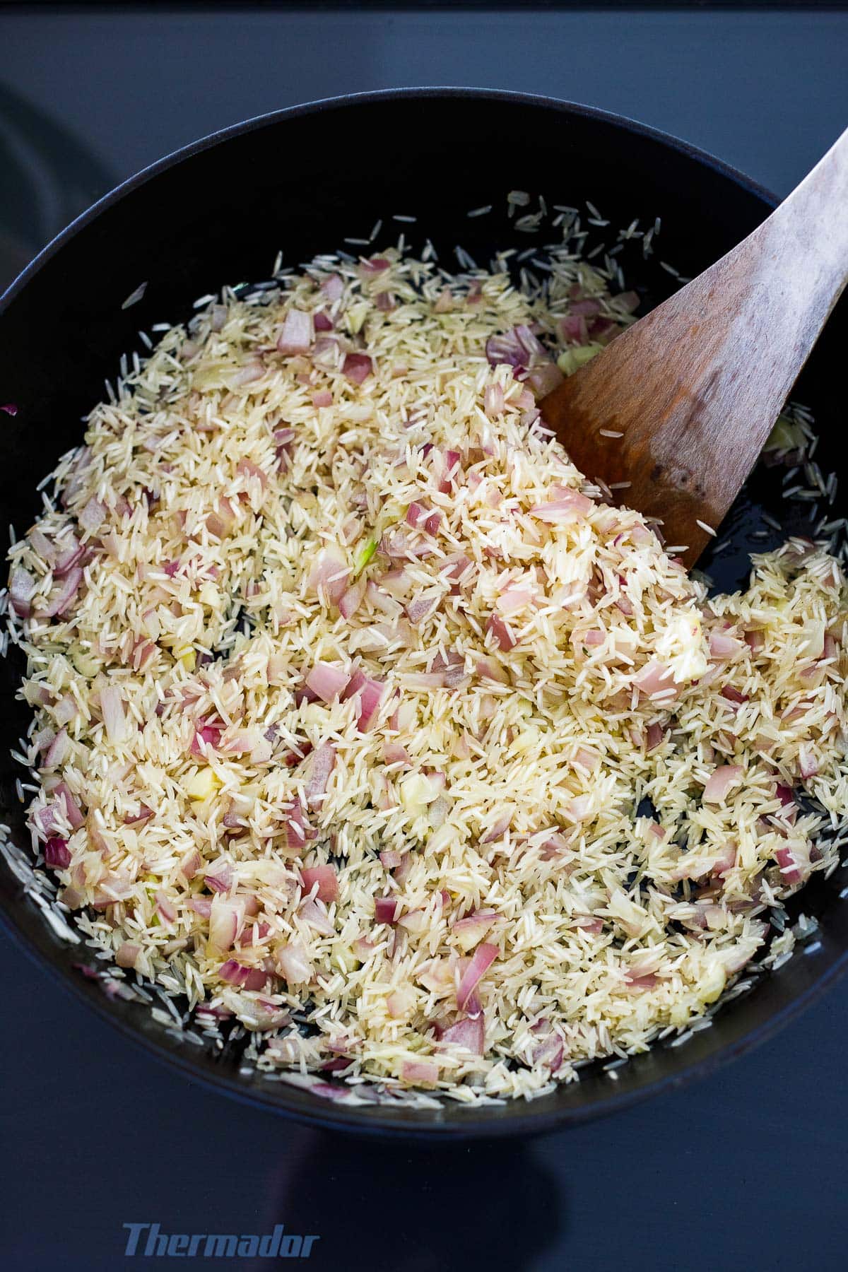 wood spatula toasting basmati rice and onions in a sauté pan.