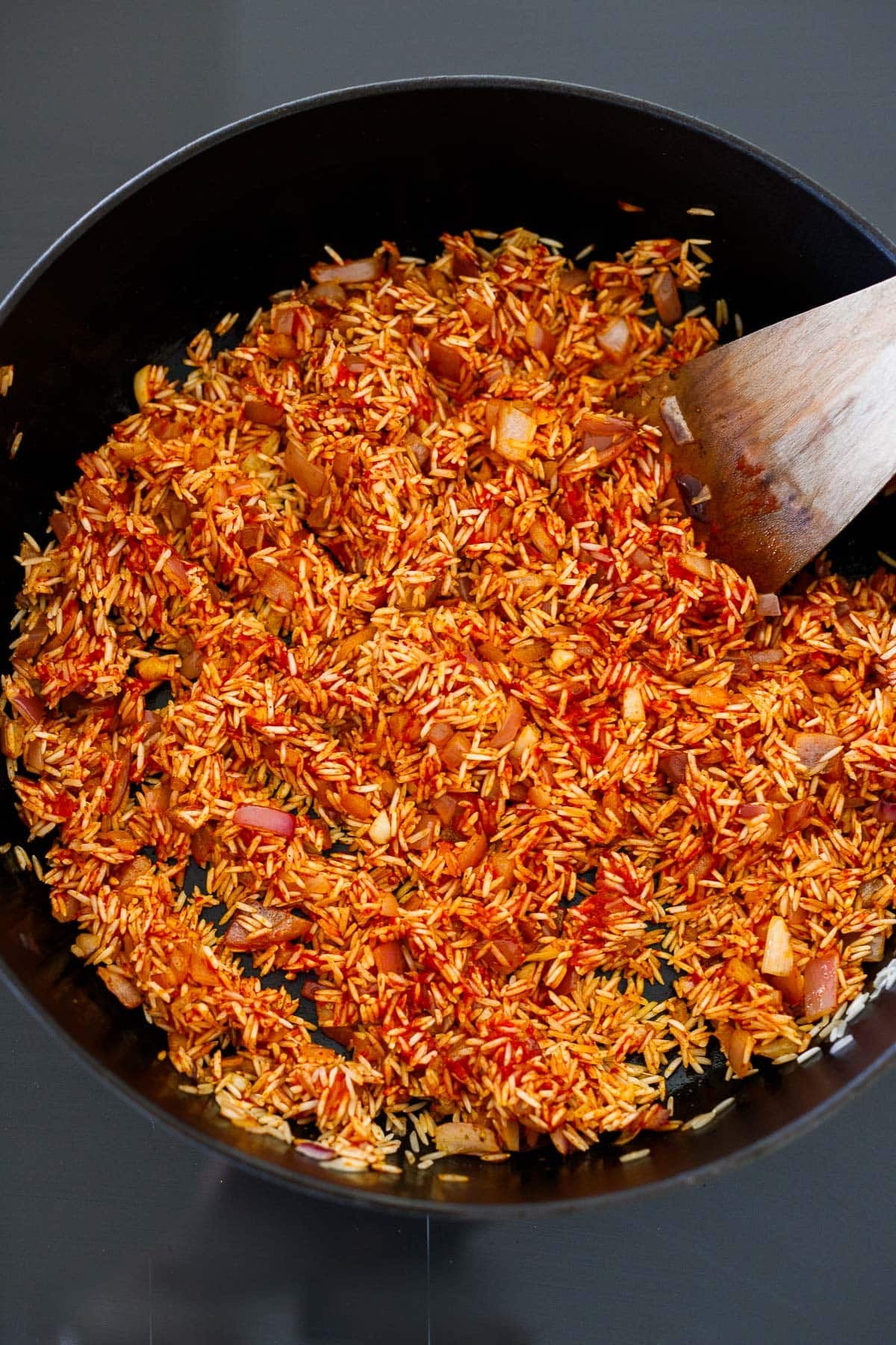wood spatula stirring seasoned spanish rice before liquid is added. 